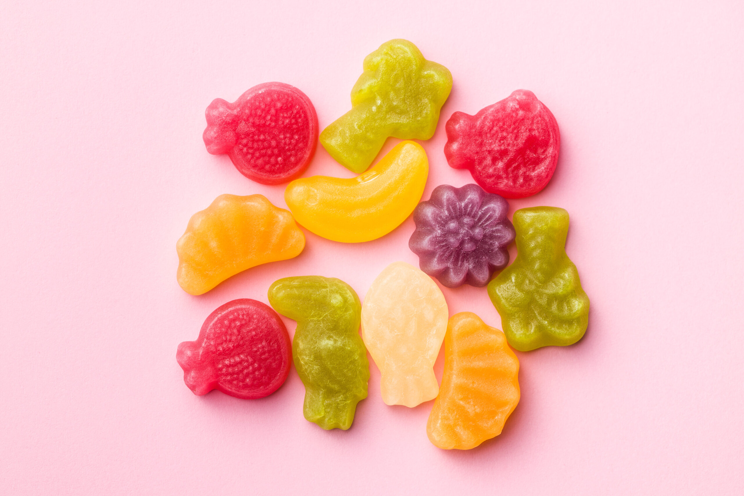 Rainbow fruit gummy candies on a pink paper.