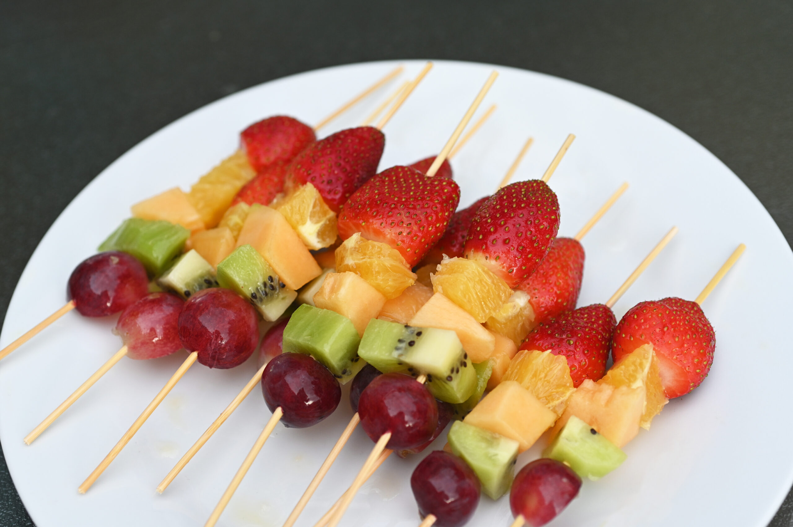 A plate featuring some fresh rainbow fruit skewers. 