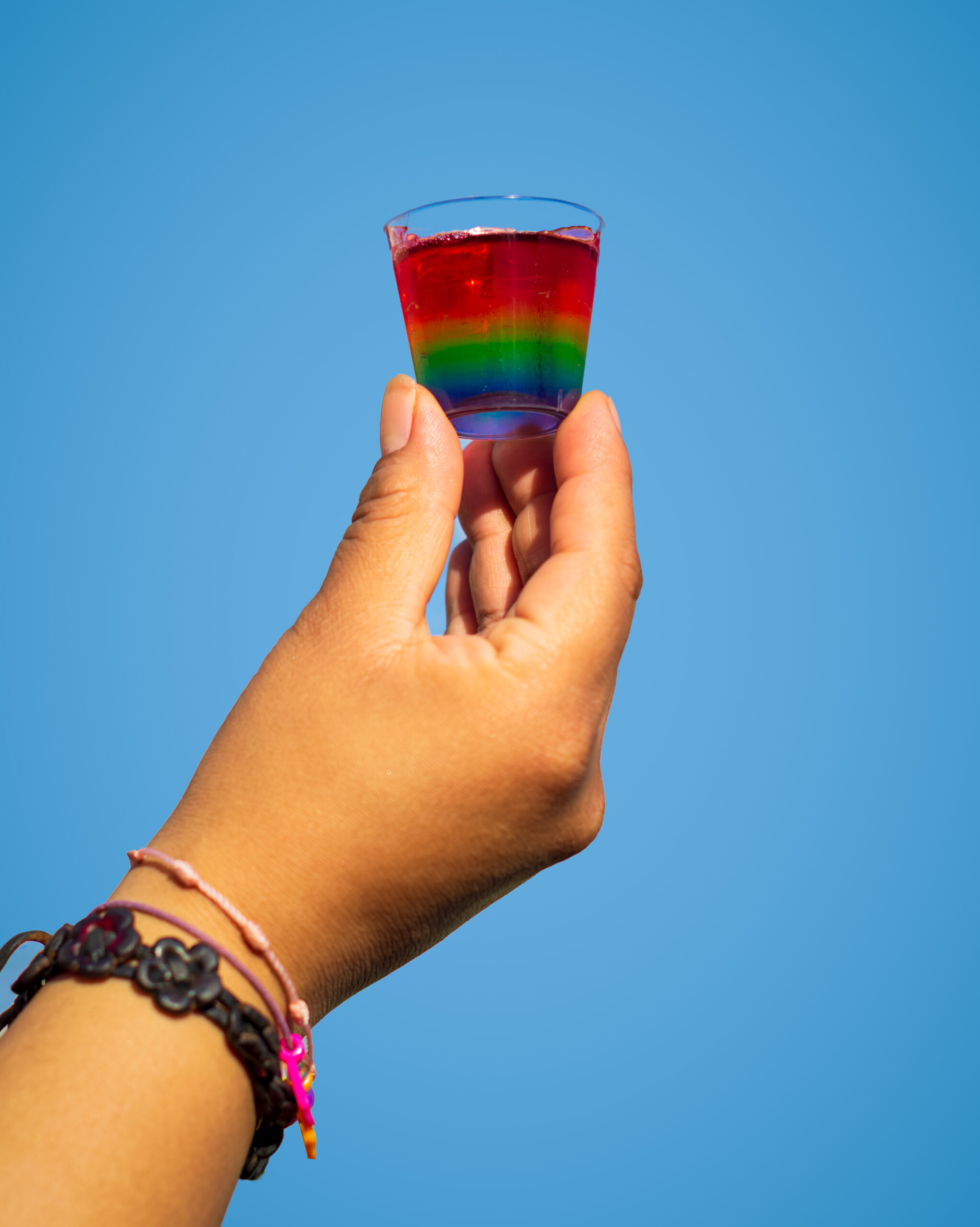 Rainbow,Jello,Shot. Isolated hand holding a rainbow jello shot on a blue background