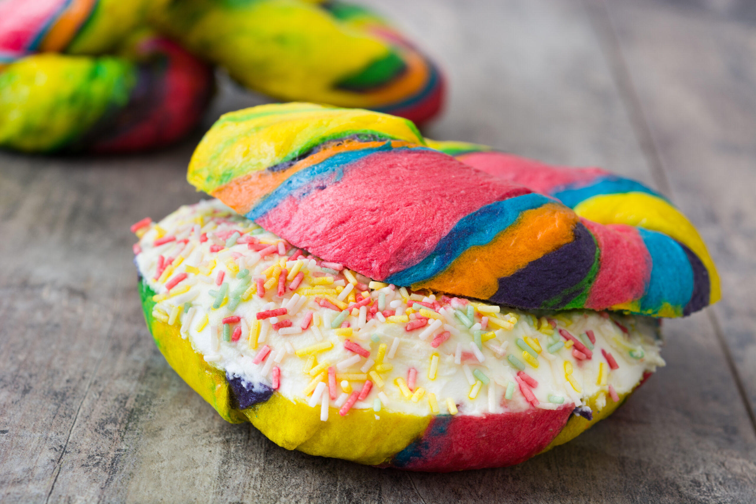 Zoom-in picture of rainbow bagels resting on a wooden surface. 