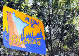 Road sign says "Welcome to Minnesota" with trees behind