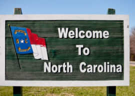 "Welcome to North Carolina" on a wooden sign with the state flag on it