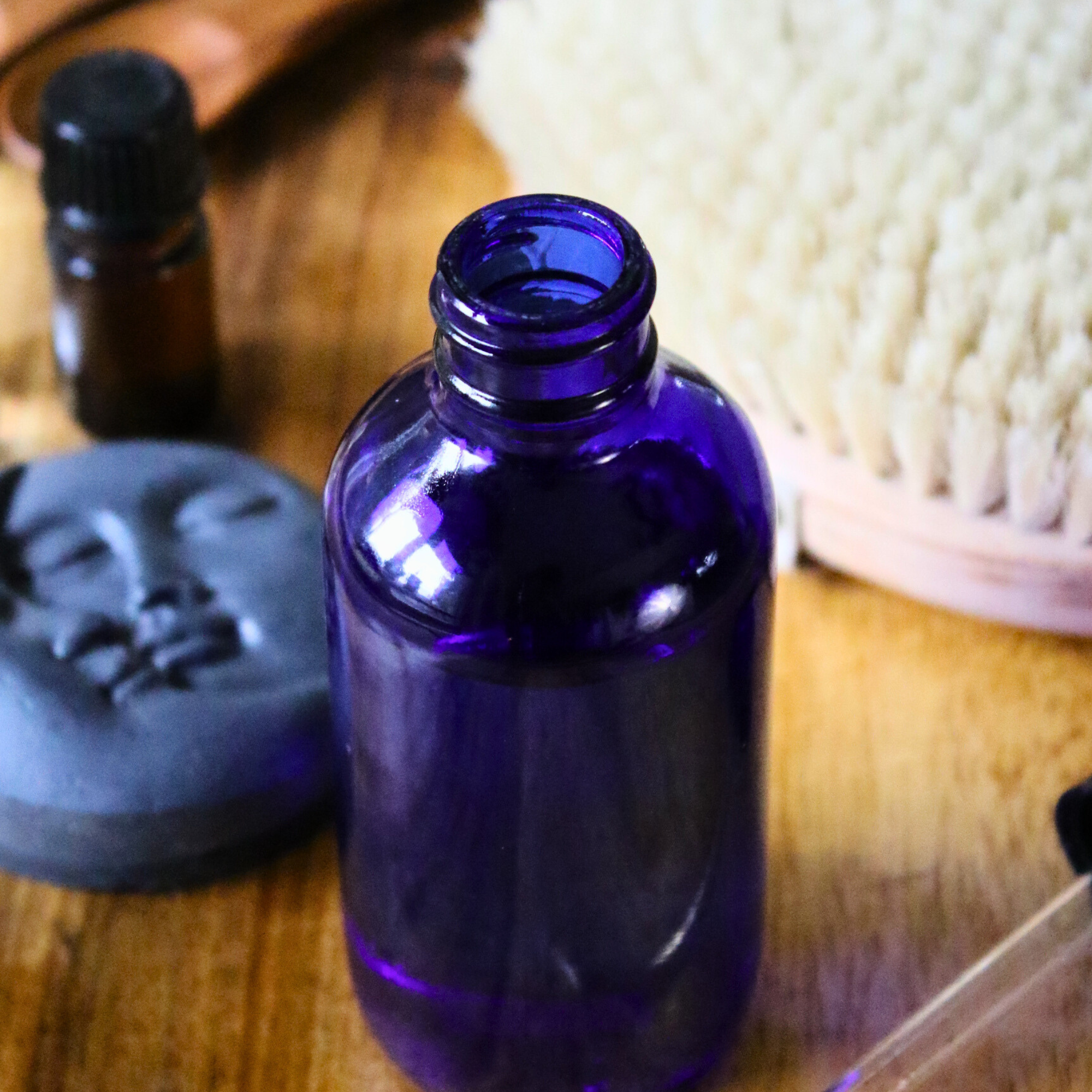 A blue bottle of bath oil next to charcoal soap, essential oils, and a dry skin brush.