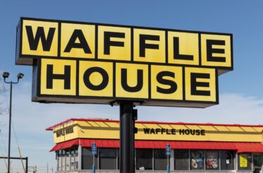 Waffle House sign in front of a Waffle House restaurant and cloudy blue skies