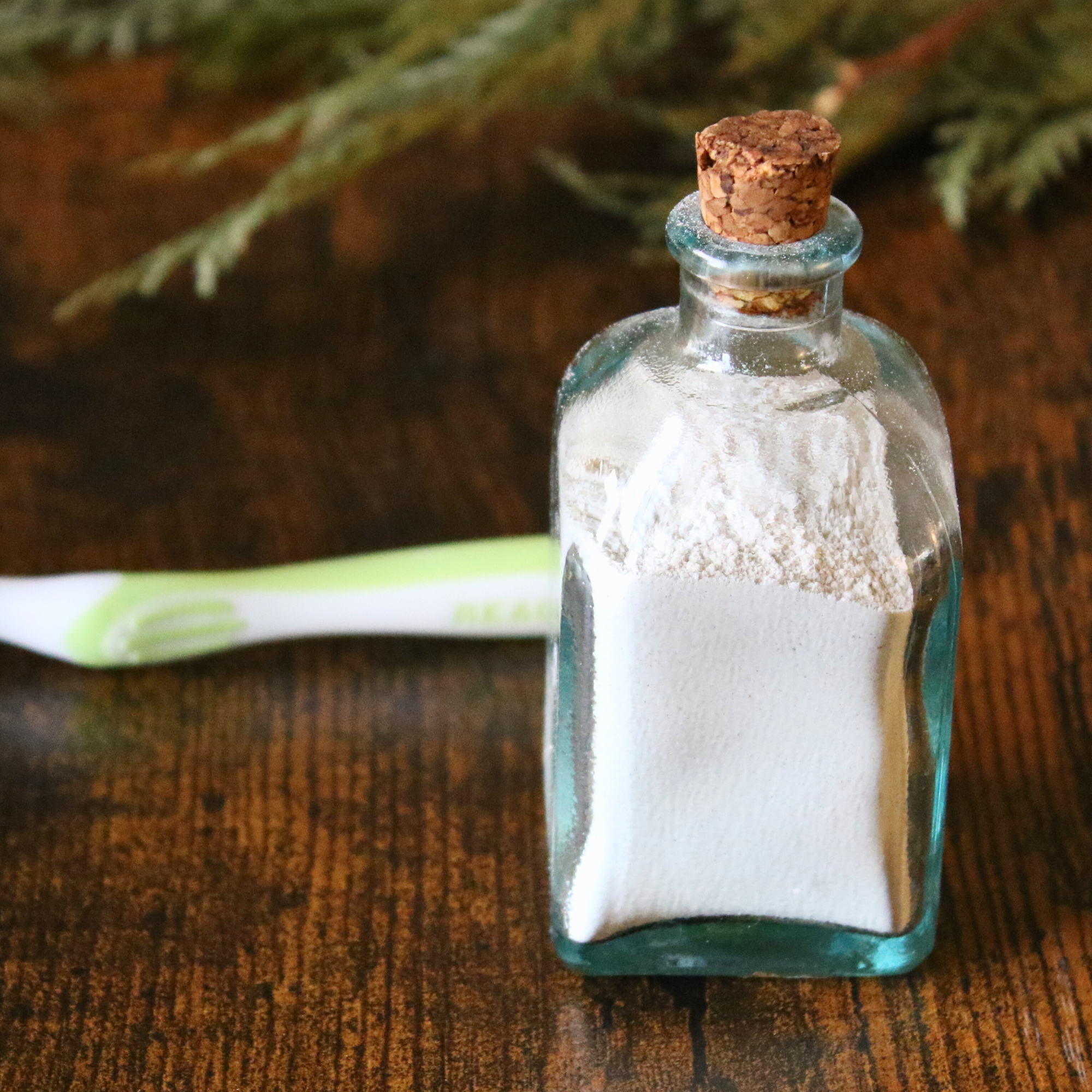 A glass bottle of tooth powder next to a toothbrush.