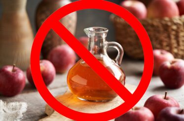 Glass pitcher of apple cider vinegar on a table surrounded by apples, with a red "cancel" sign superimposed over it all.