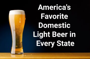 Tall glass of light beer with foam on a wooden surface against a dark background.
