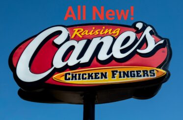 Raising Cane's Chicken Fingers sign with "All New!" written above it in orange letters