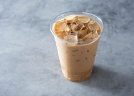 Plastic cup filled with iced coffee on gray surface
