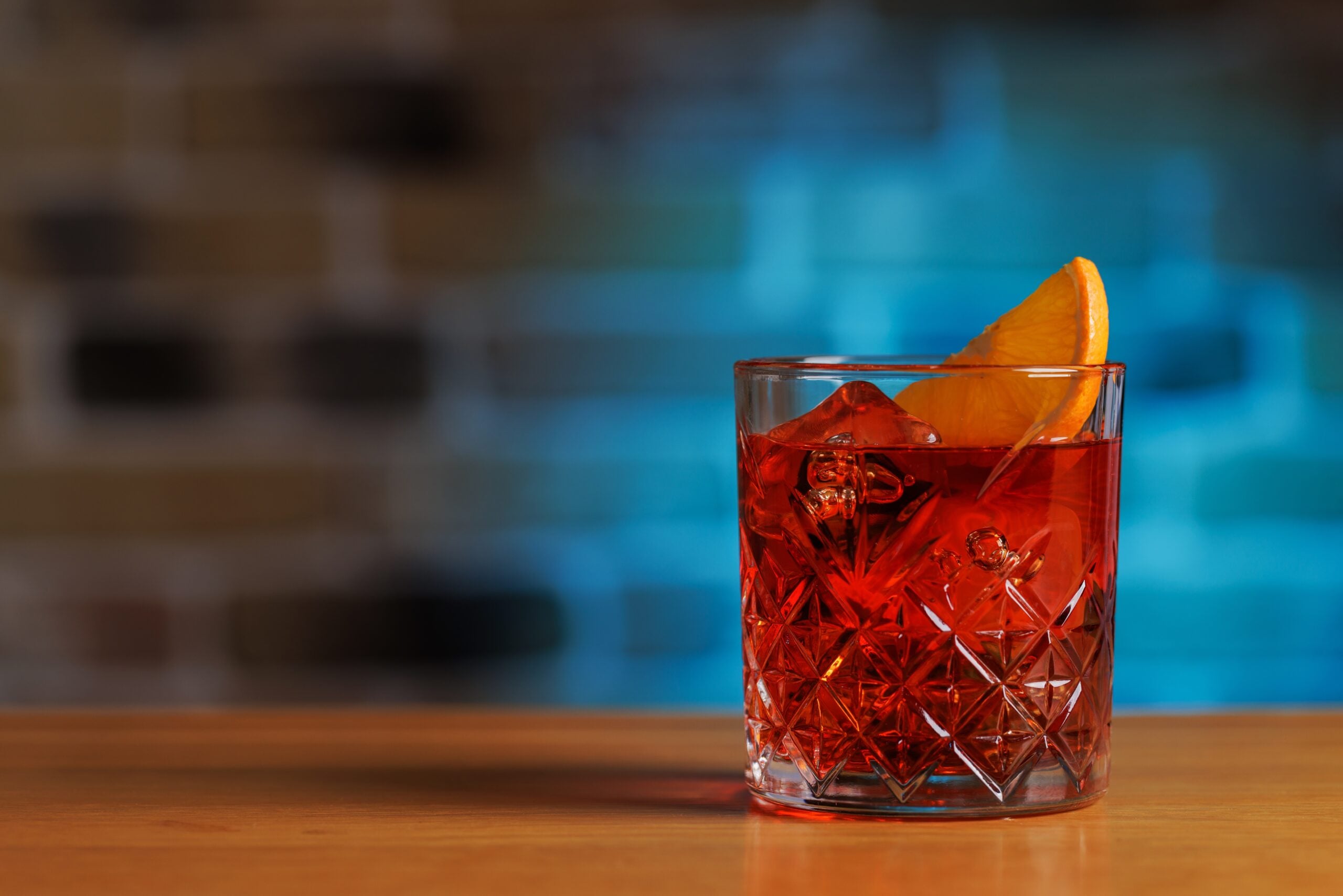 A classic Negroni cocktail against a blurred, blue backdrop. 