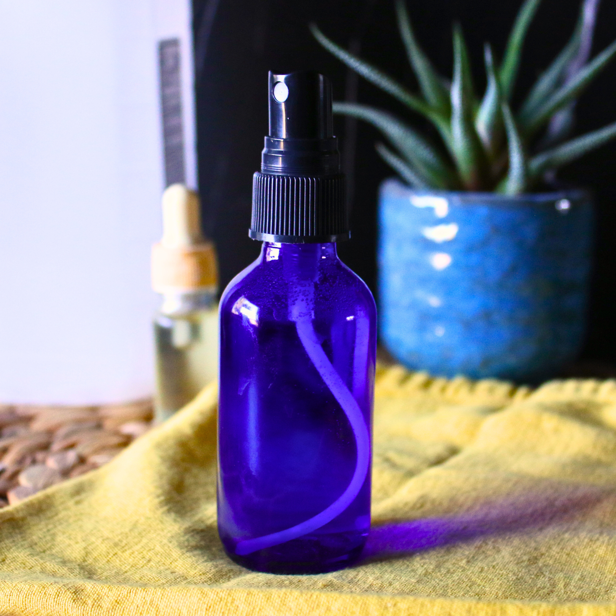 Linen spray in a blue glass bottle next to a bottle of essential oils and rubbing alcohol. 