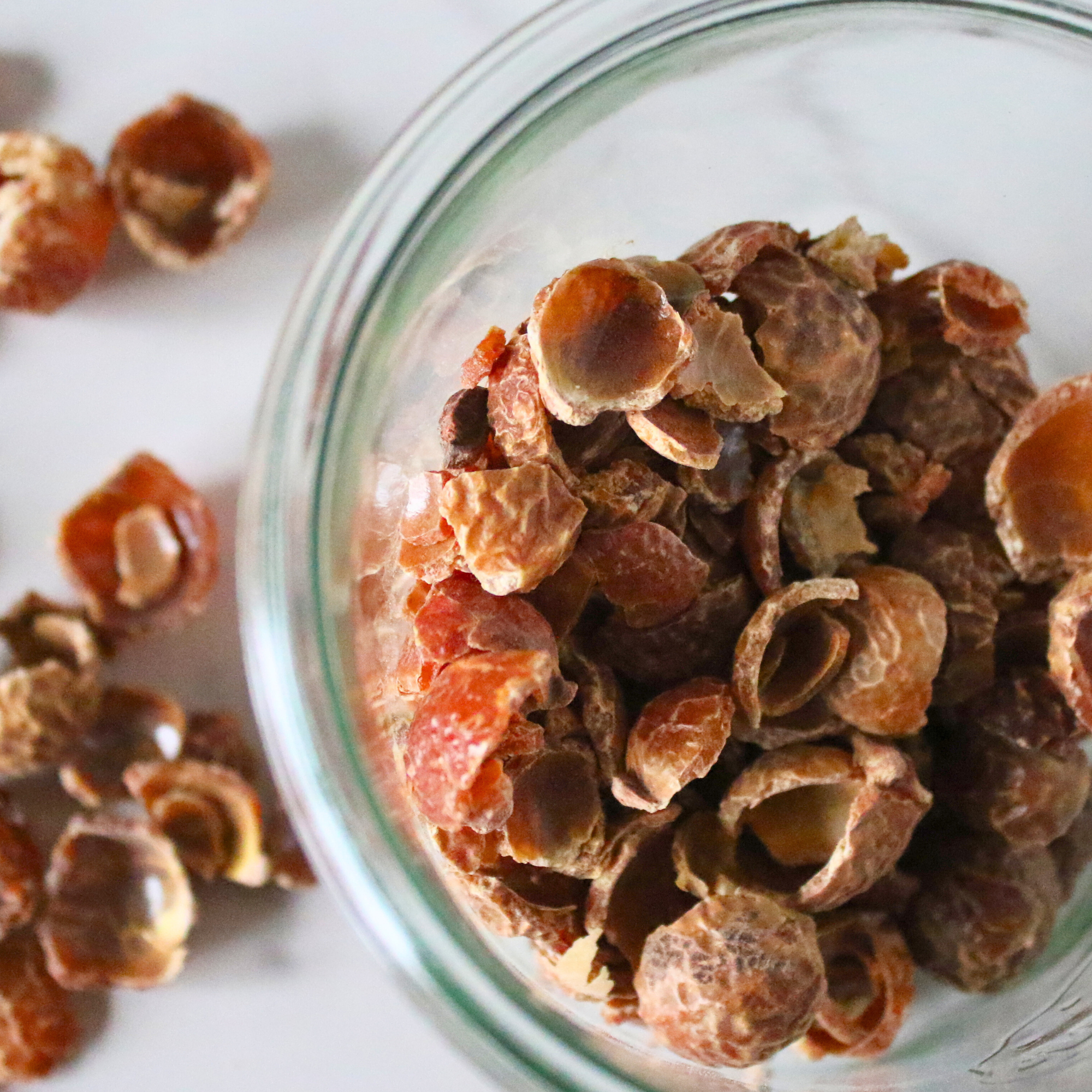 A glass jar of soap nuts poured out on a countertop. 