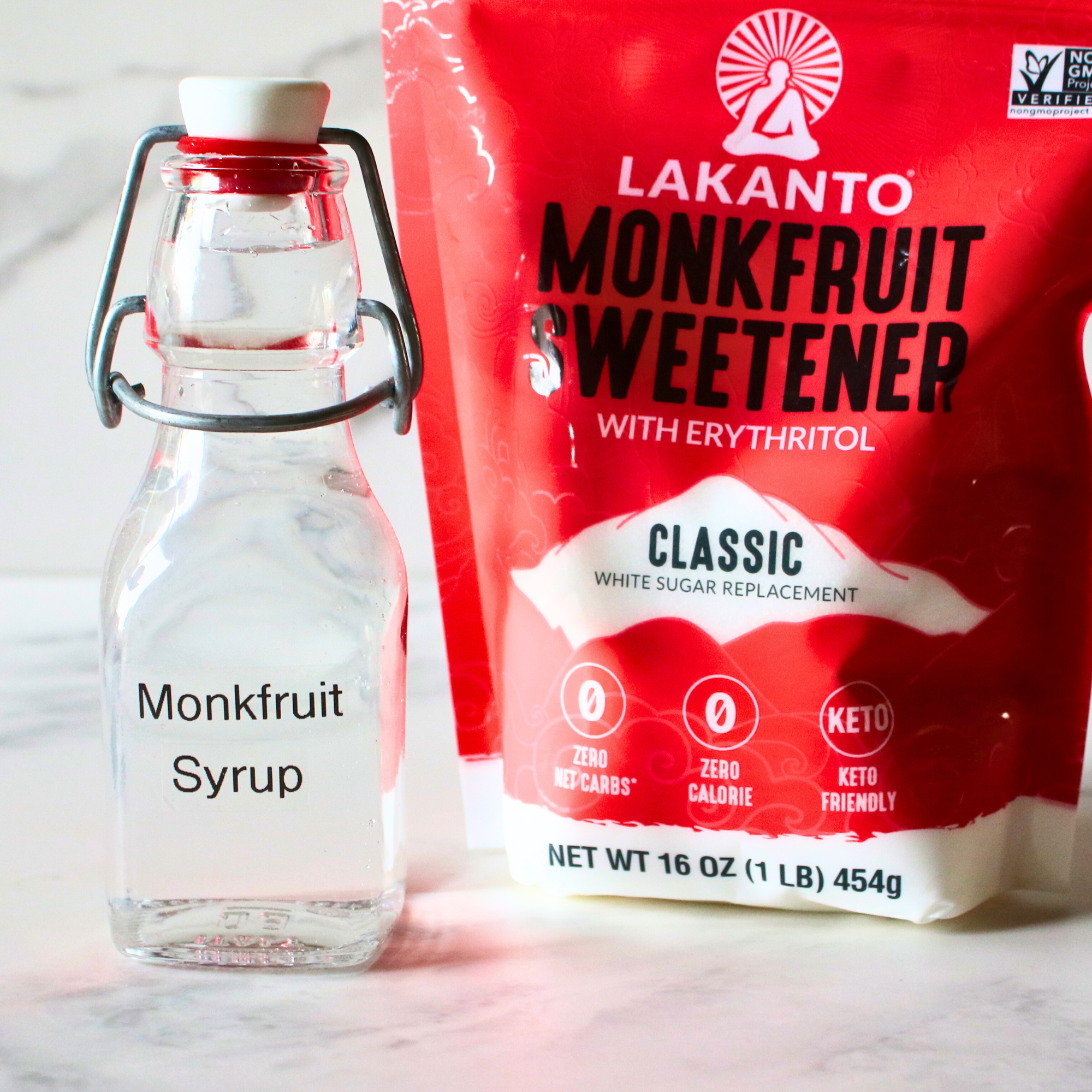 A small glass flip top bottle labeled monk fruit syrup next to a bag of monk fruit sweetener.