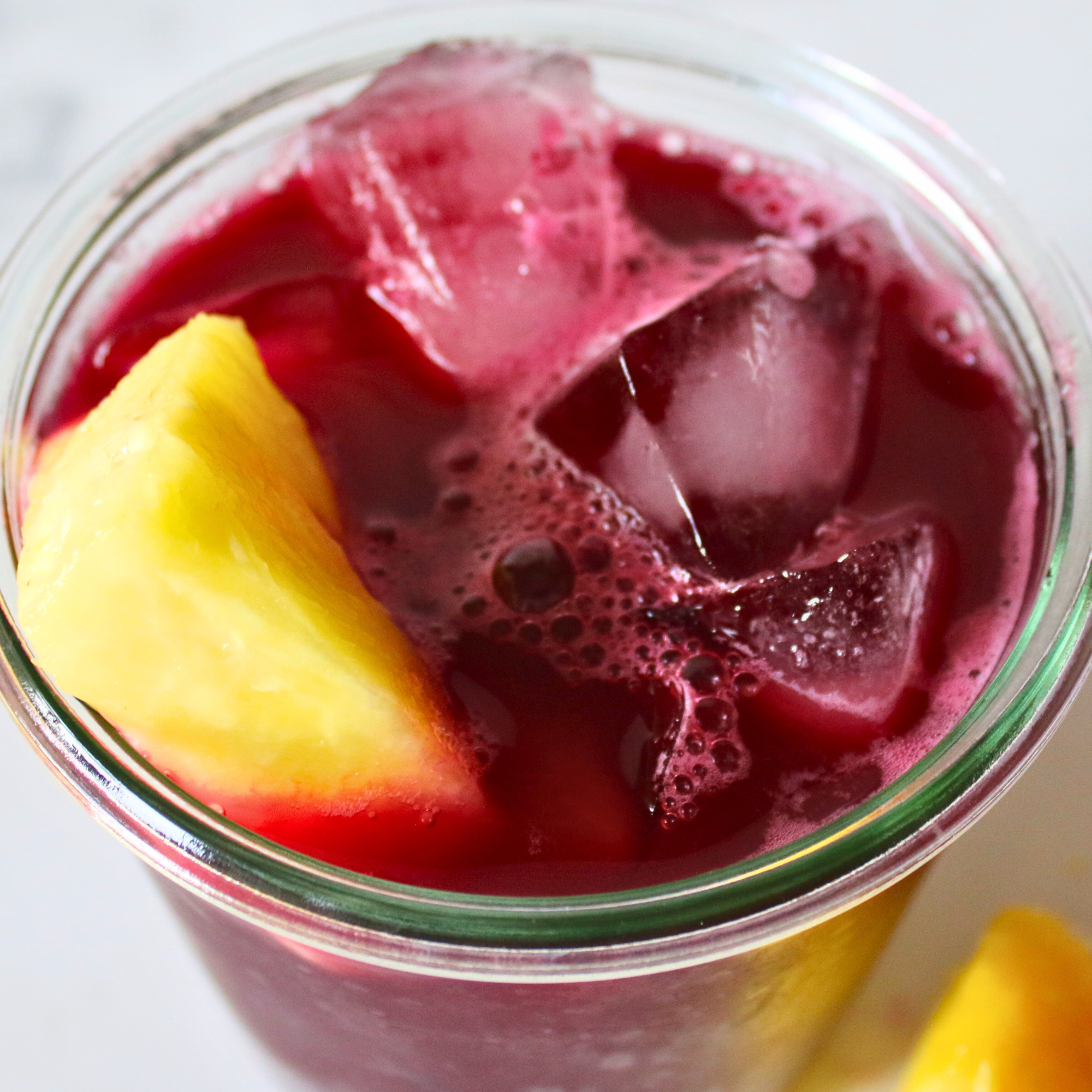 A cup of red cranberry juice with pineapple chunks on a white counter.