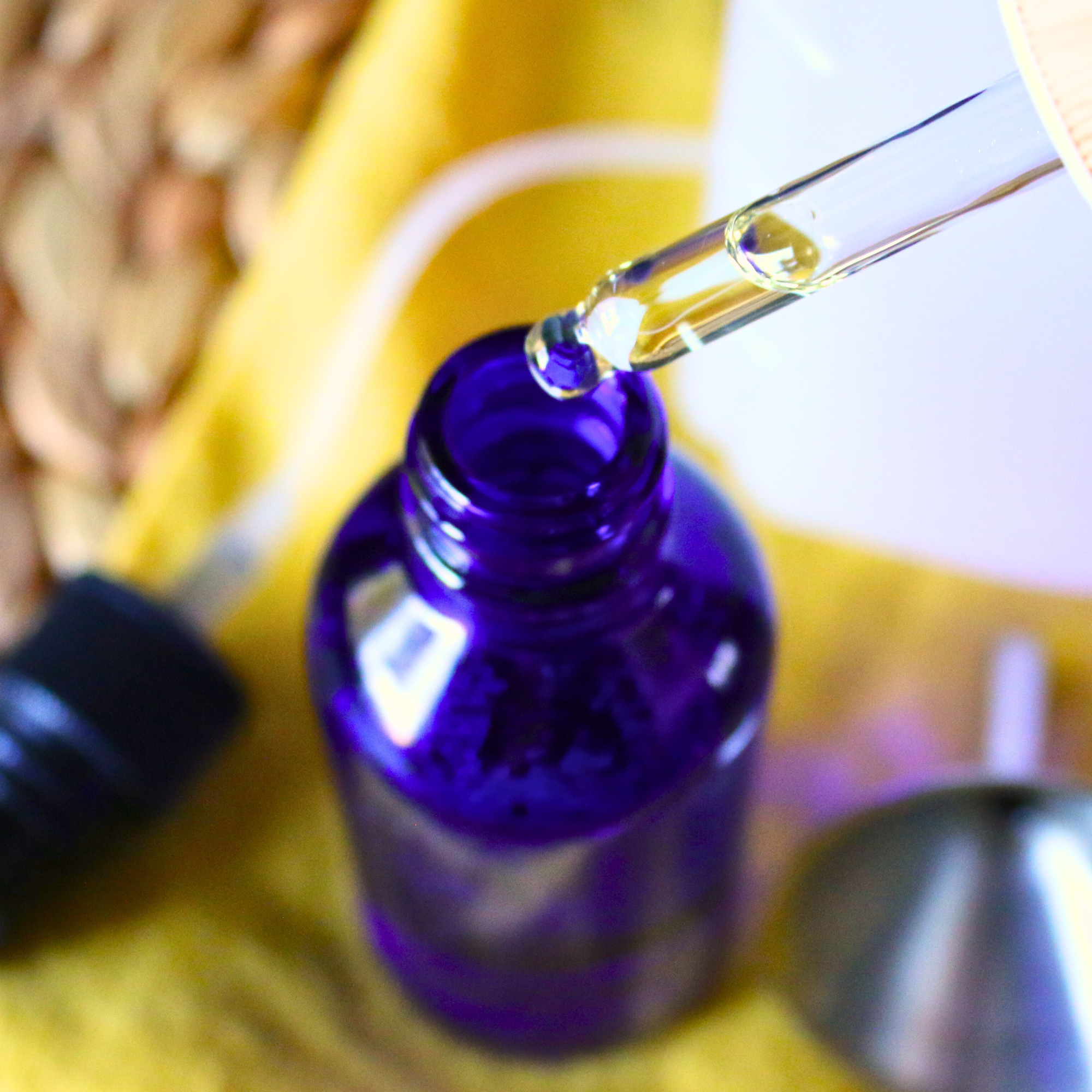 A dropper bottle of essential oils, dropping into a blue glass bottle.