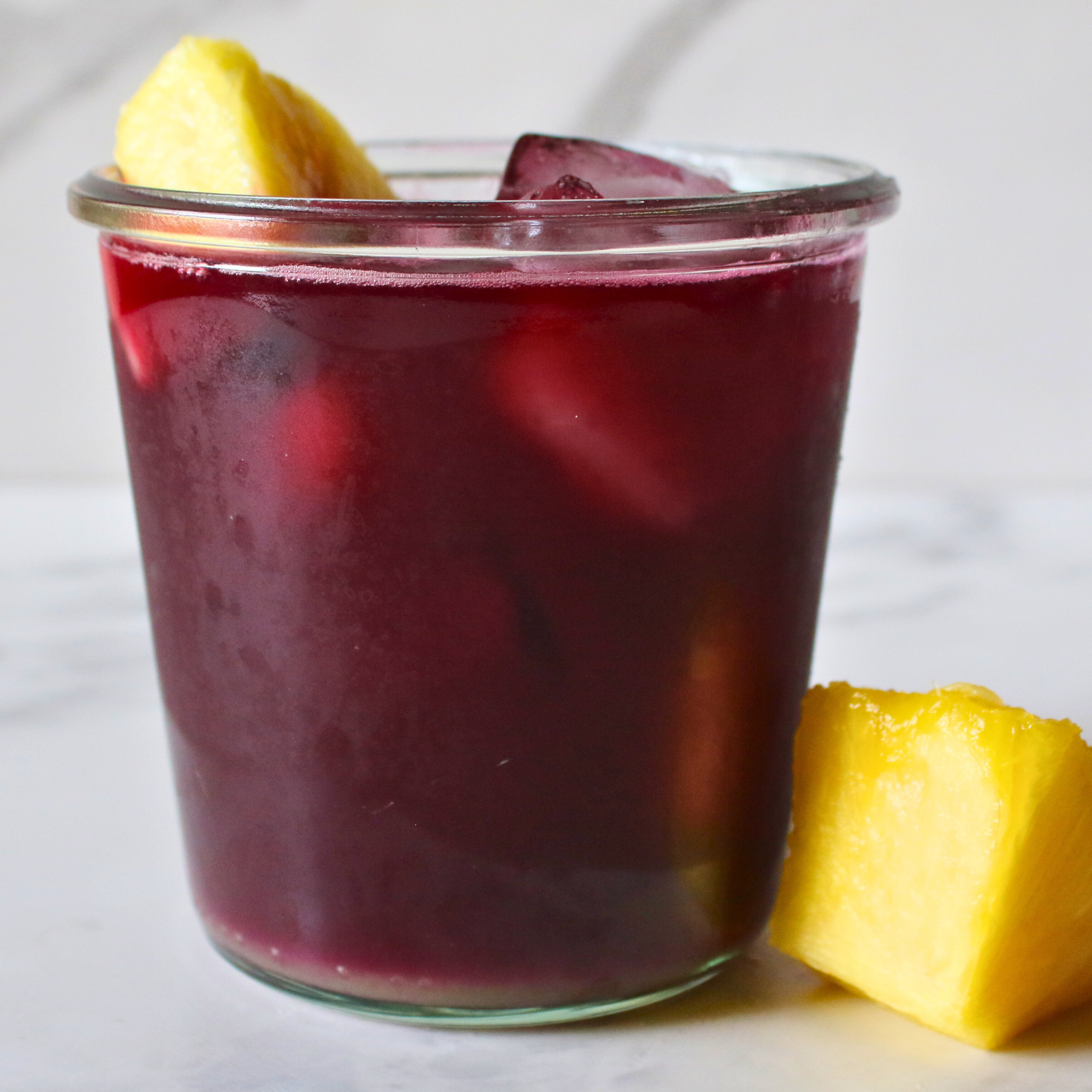 A glass jar of cranberry, pineapple, and apple cider vinegar, garnished with fresh pineapple.