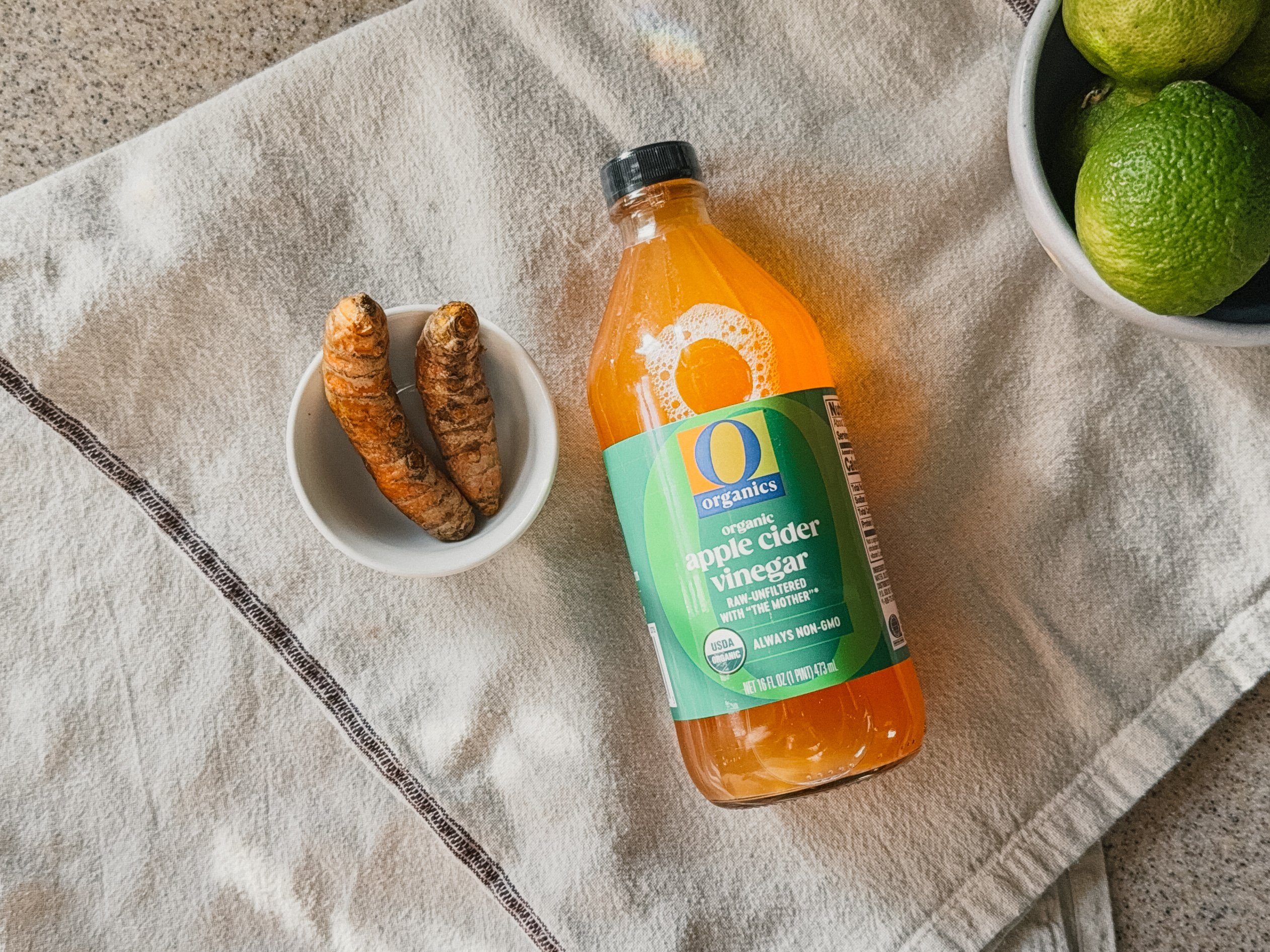 A flat lay of apple cider vinegar bottle beside turmeric root and small bowls showcasing natural ingredients
