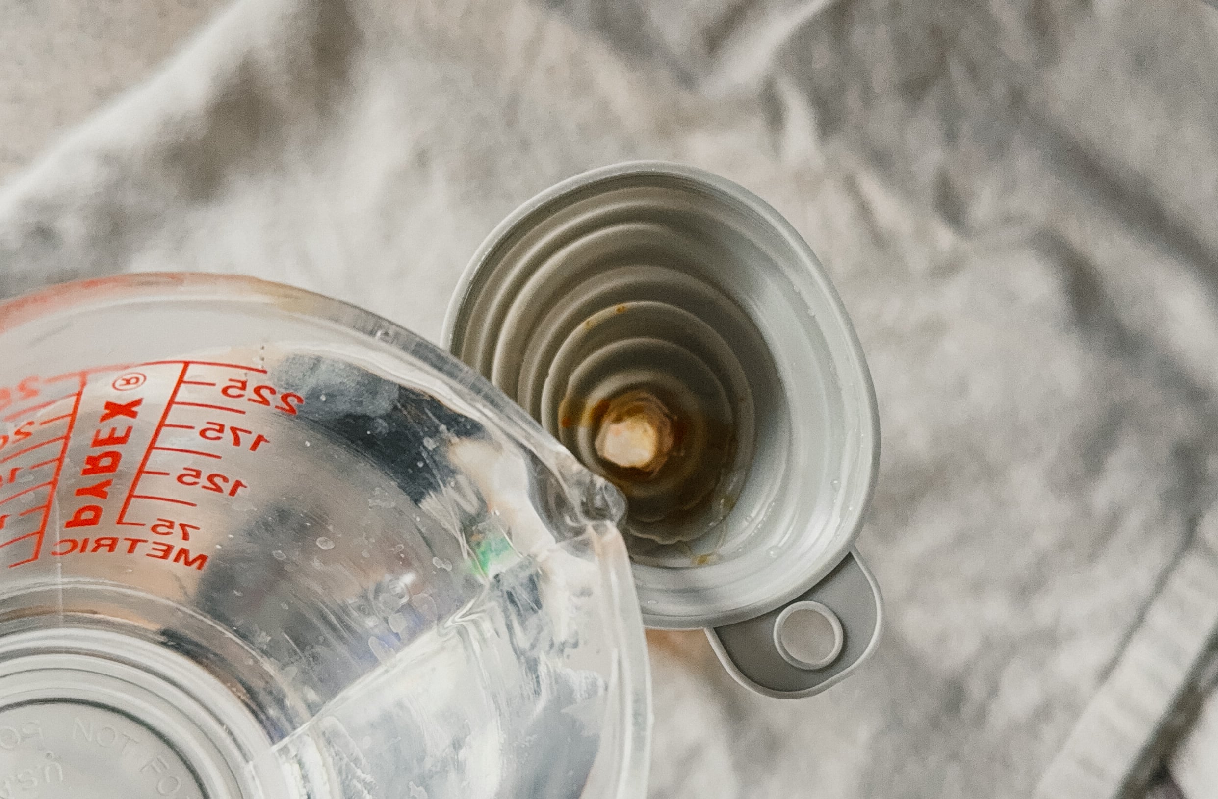 Water being poured from a measuring cup through a funnel into a bottle.