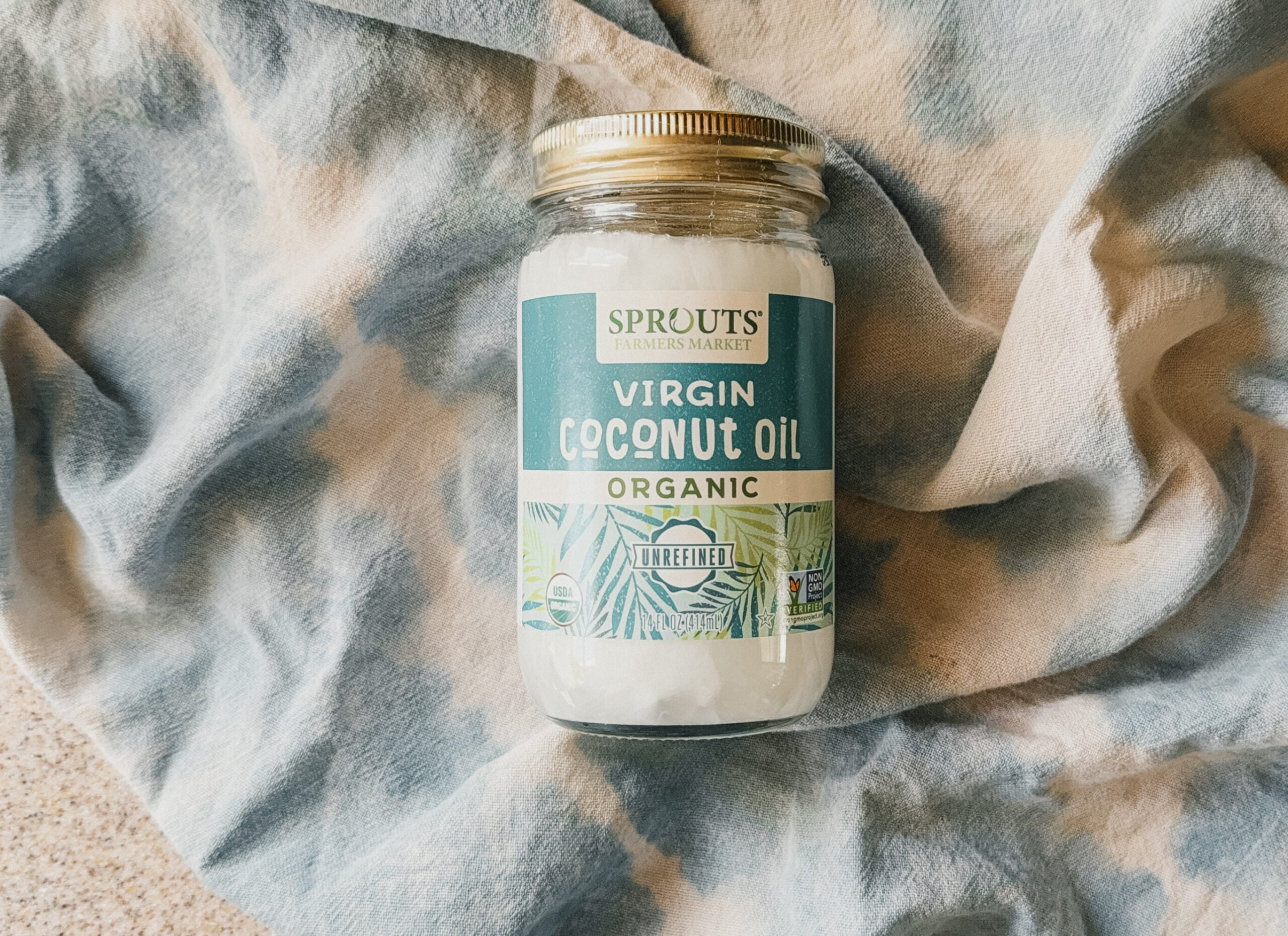 A jar of coconut oil on top of a blue tea towel.