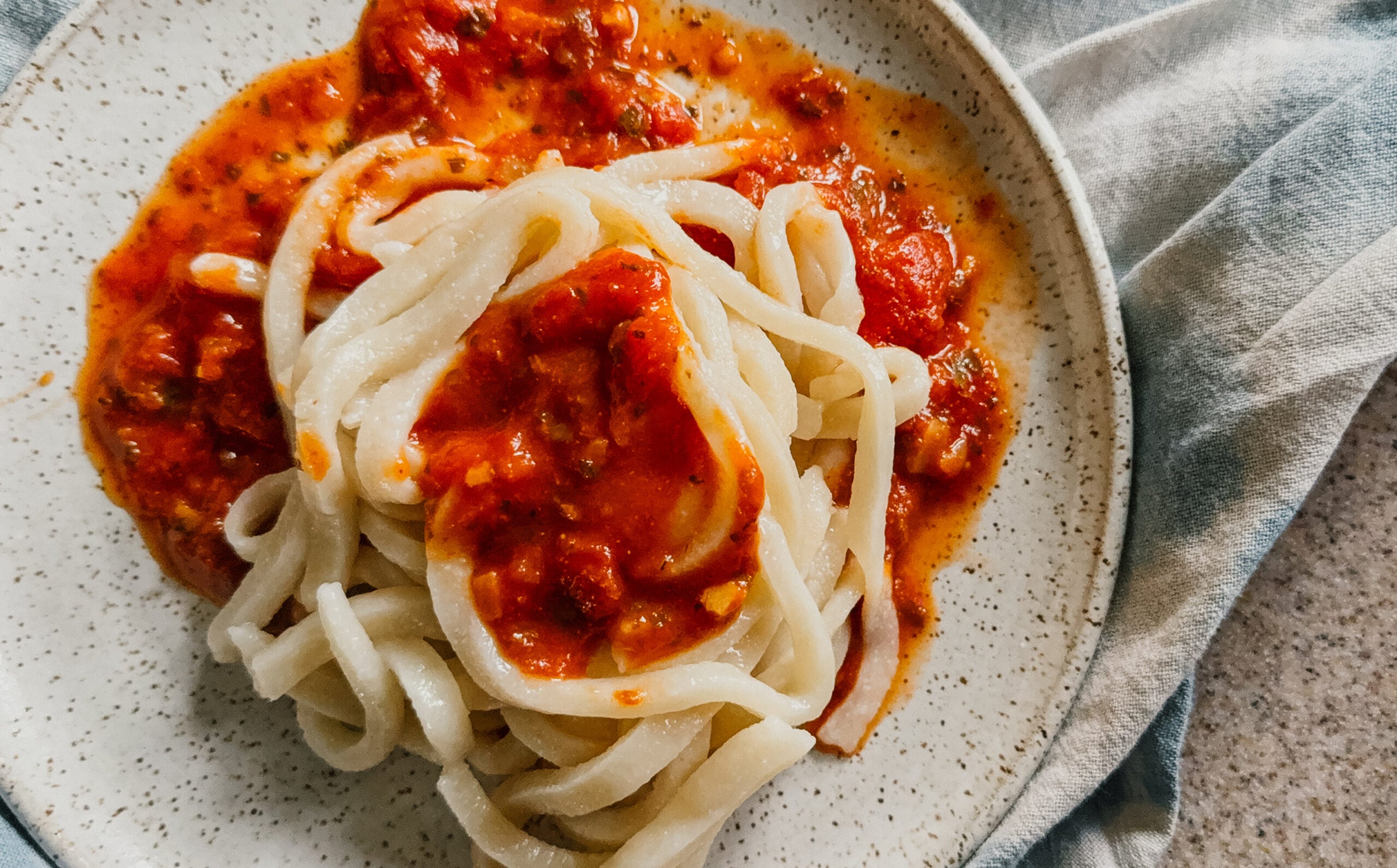 A plate of freshly cooked noodles with red sauce. A blue tea towel sits underneath.