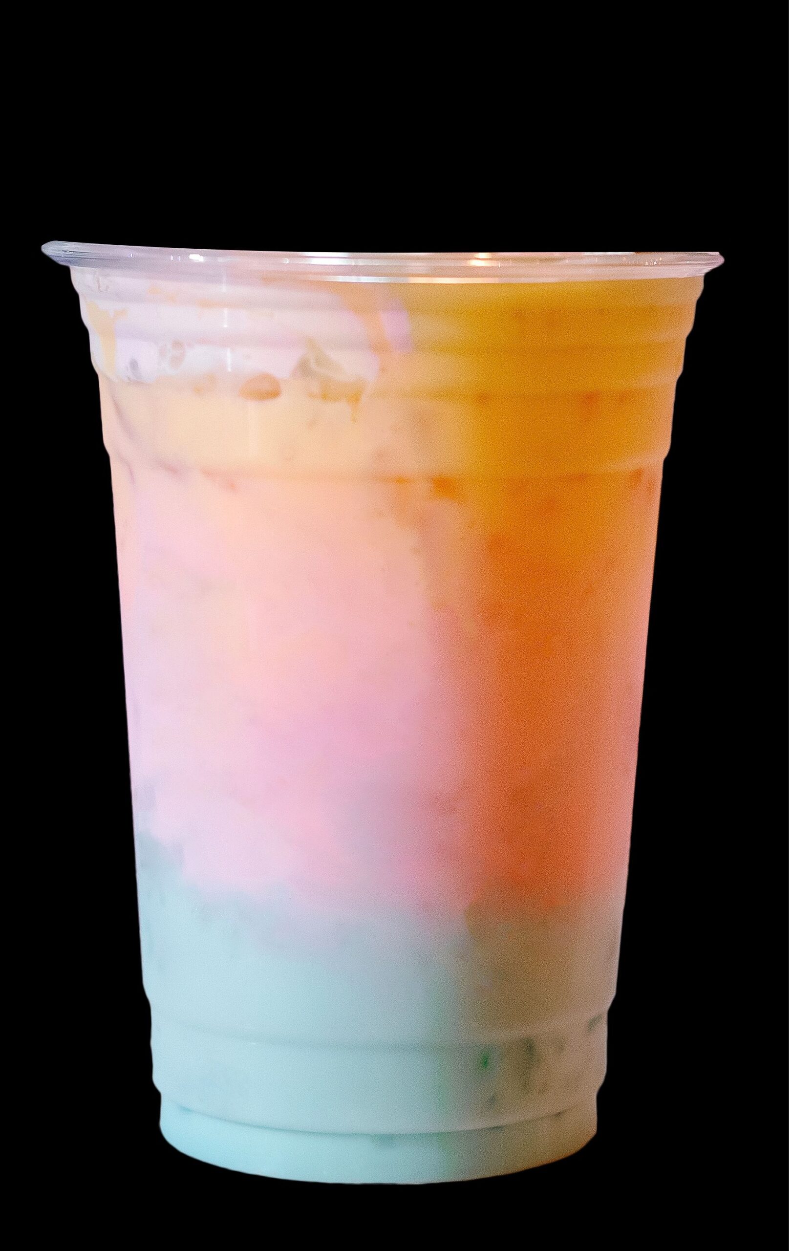 A dark backdrop featuring a glass of rainbow milkshake. 
