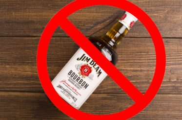 Jim Beam bottle on wooden background with a big red cancel sign over it