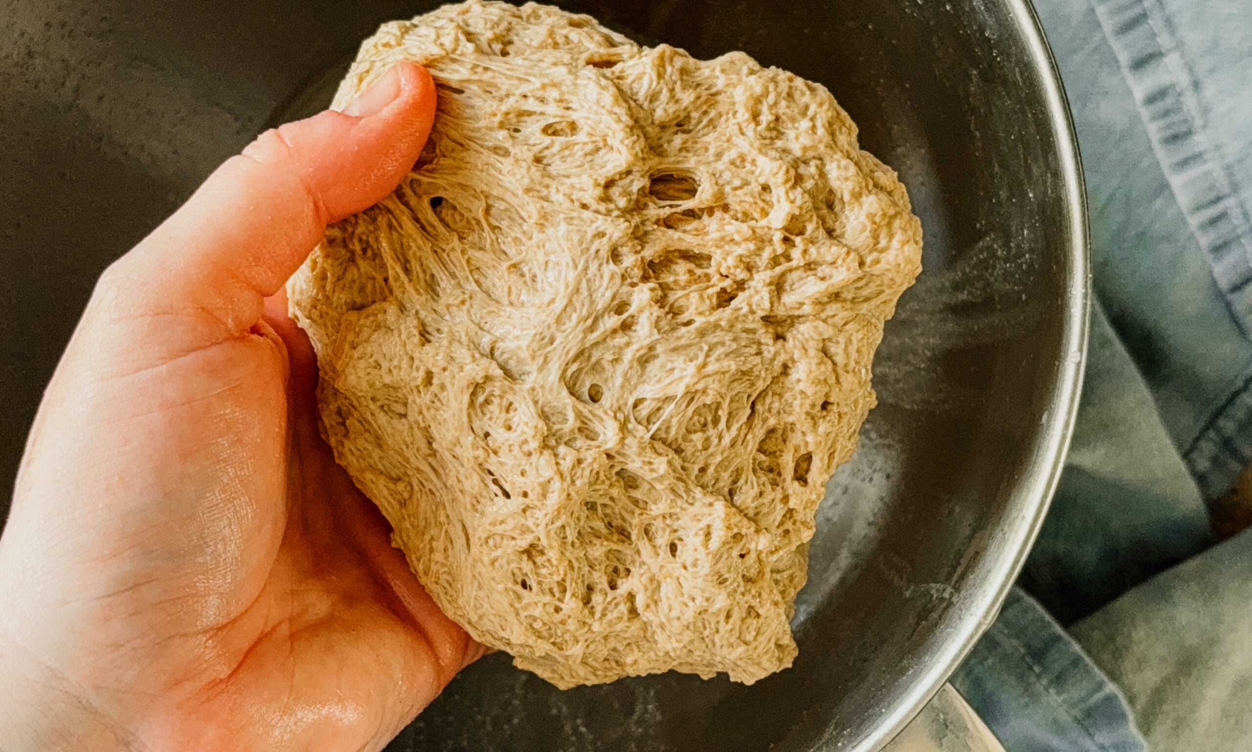 A hand holding freshly made vital wheat gluten above a silver bowl.