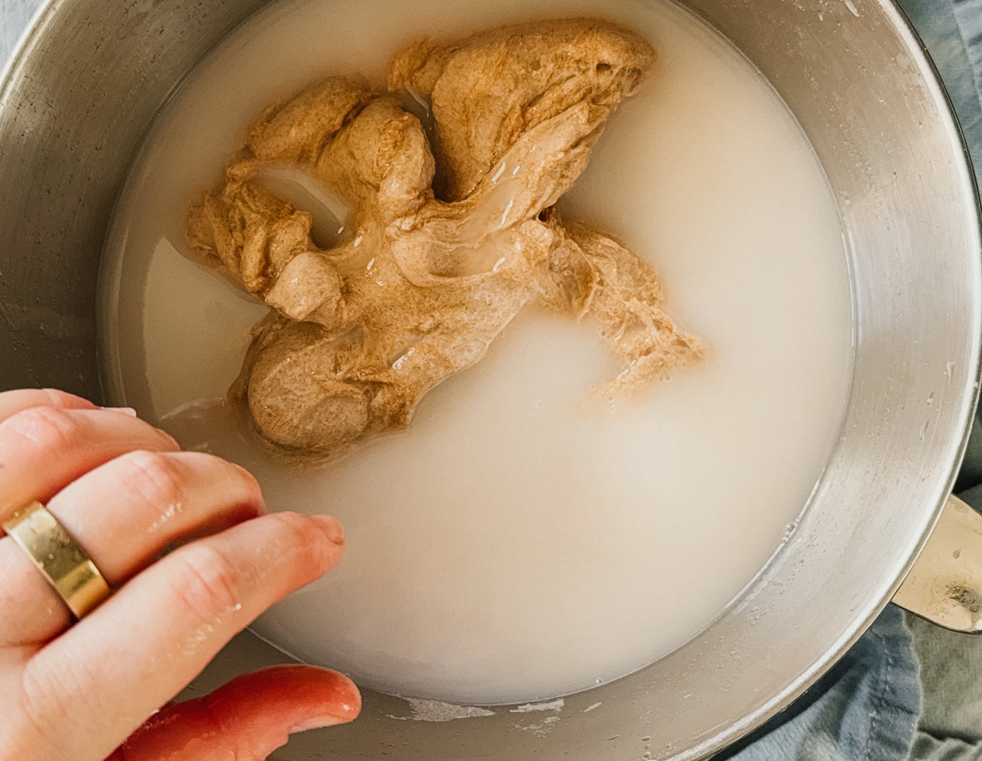 A dough ball after being kneaded in a bowl full of starchy, cloudy water. A hand rests on the bottom left side of the bowl.