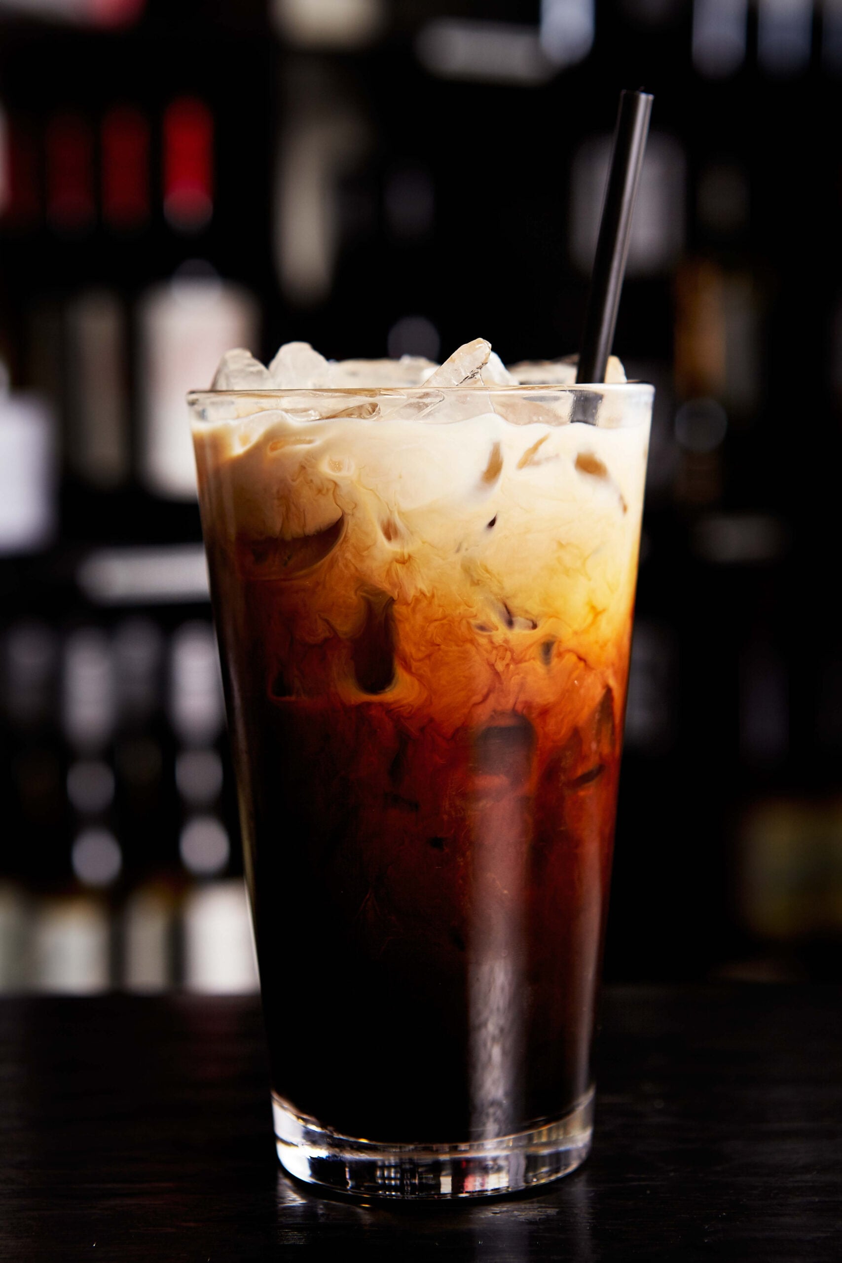 A glass of Thai iced coffee on a blurred black background. 