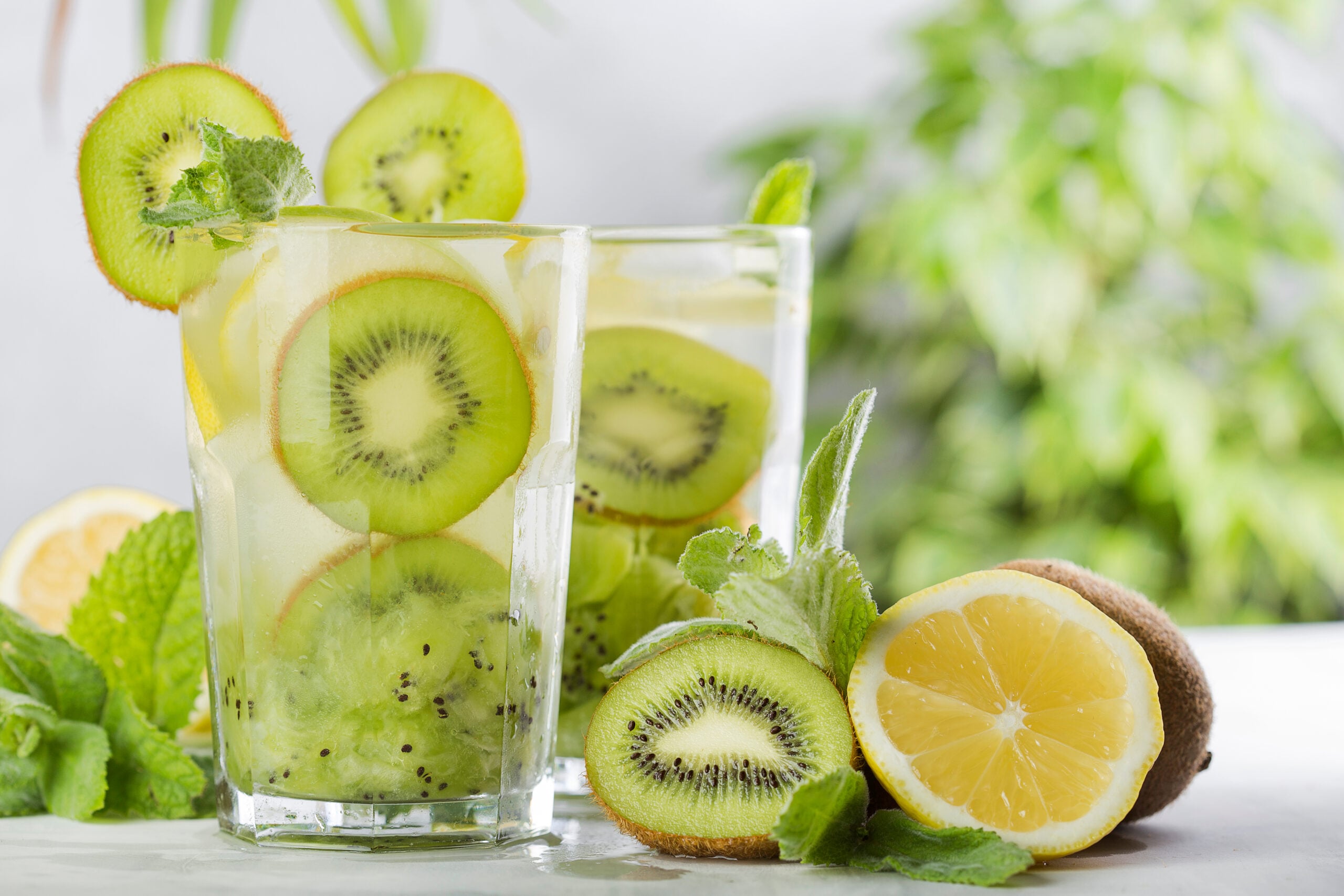 Glasses of kiwi agua fresca surrounded by its ingredients. 
