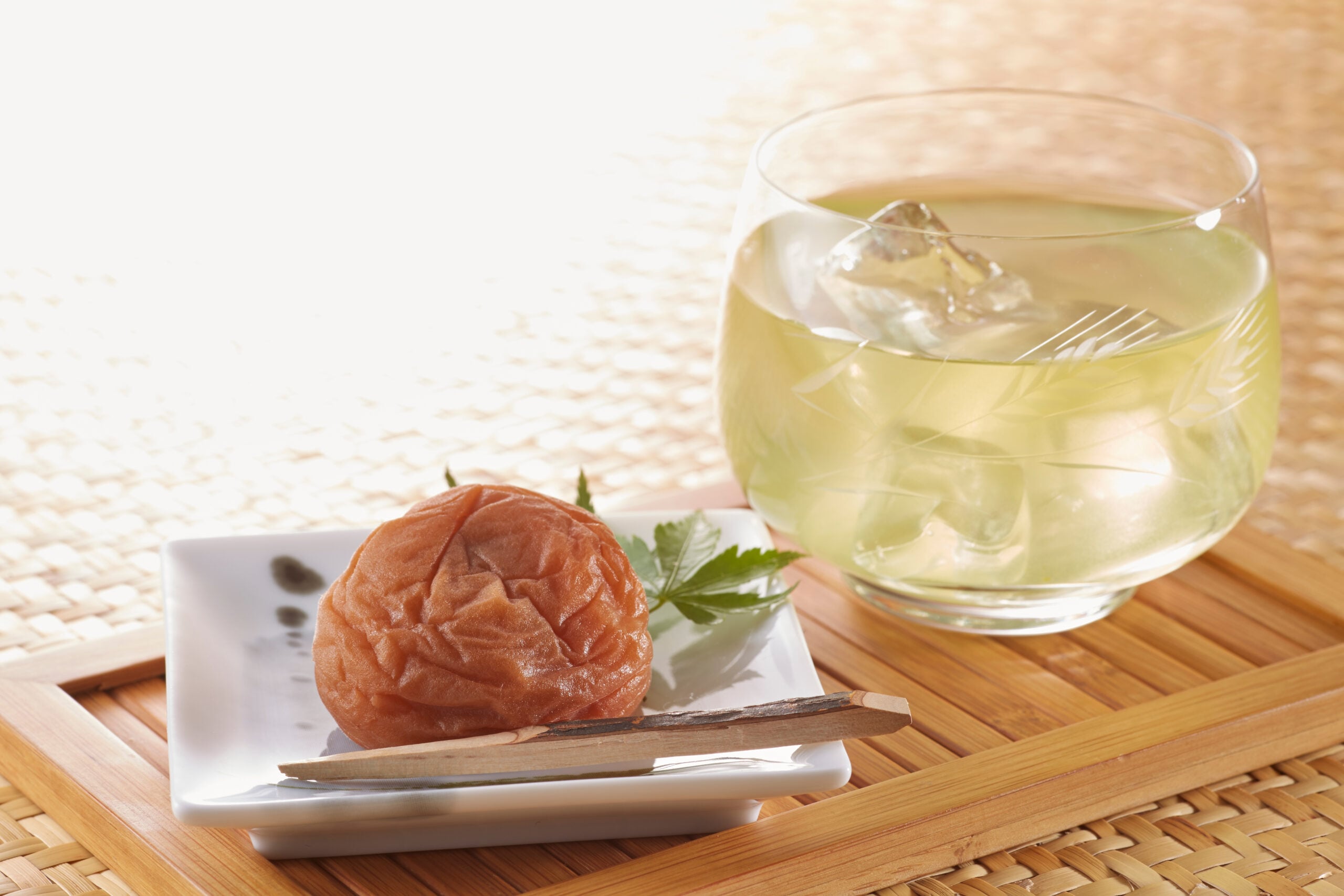 A bamboo surface displaying Japanese salt plums and iced Umeboshi tea.