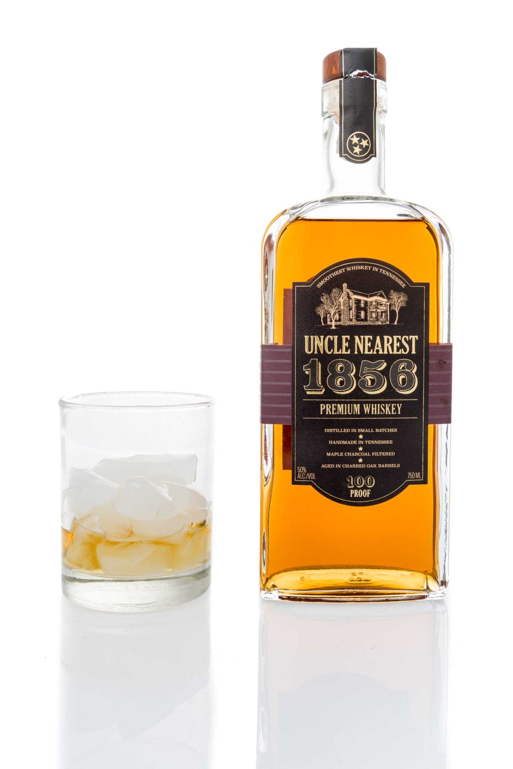 A plain white backdrop featuring a glass and a bottle of Uncle Nearest whiskey.