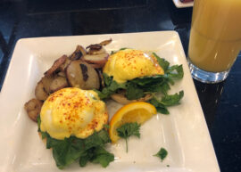 Eggs benedict with potatoes and a glass of orange juice at a Keke's