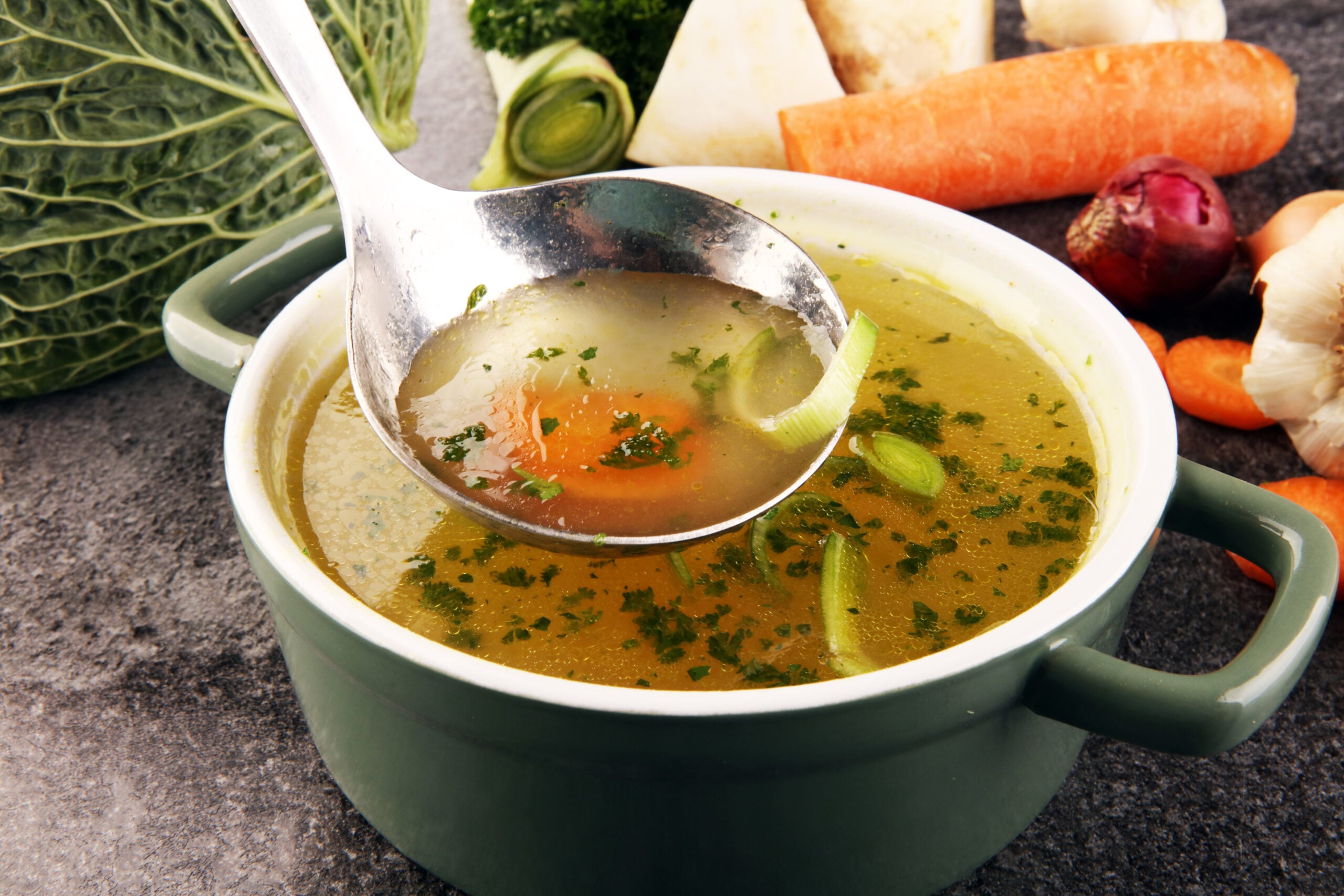 Homemade vegetable broth encircled by its ingredients. 