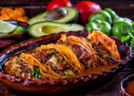 Pork carnitas tacos with sliced avocado, lime, and other veggies behind