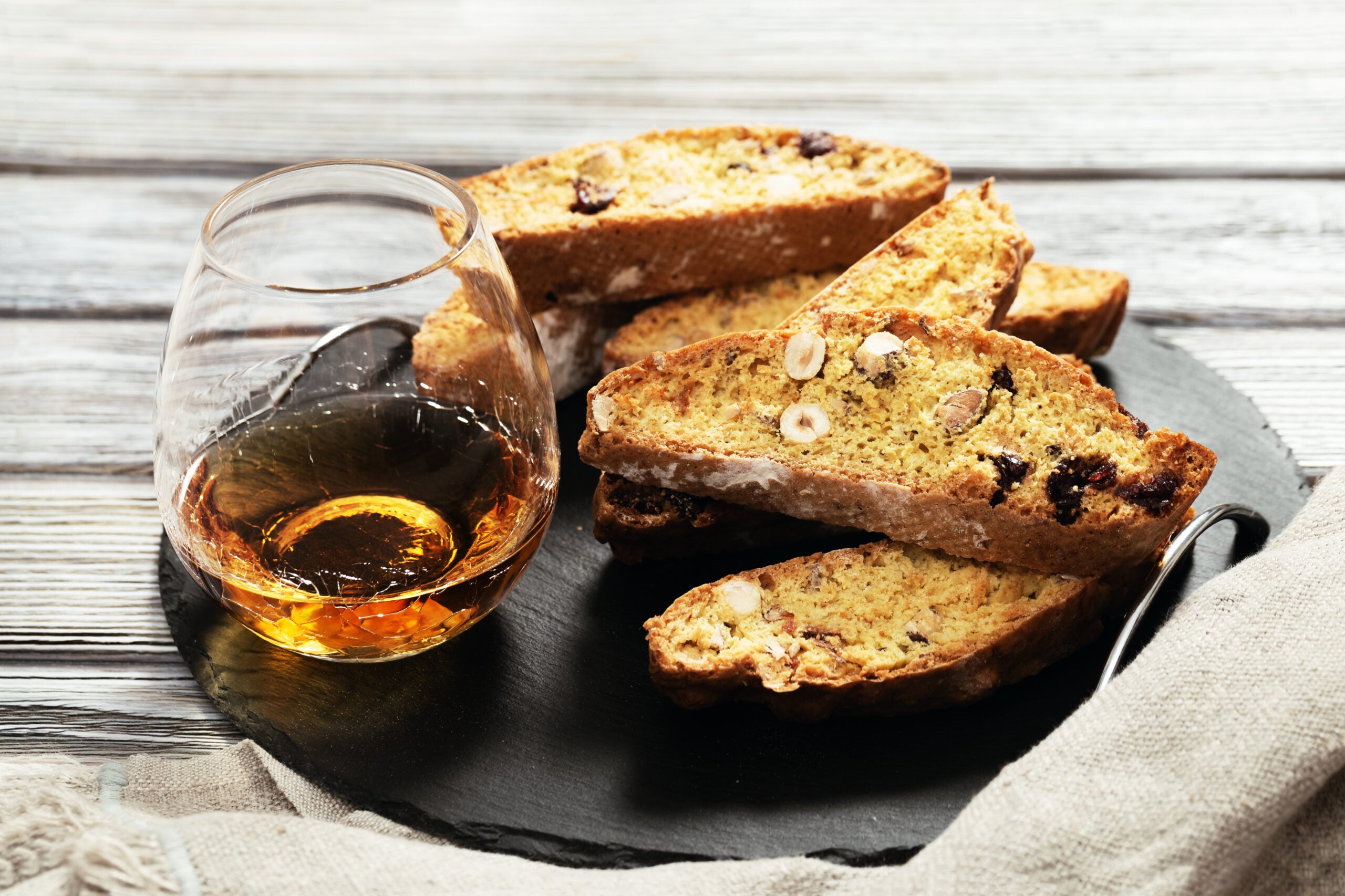  Italian biscotti cookies on a black slate and a Vin Santo glass.