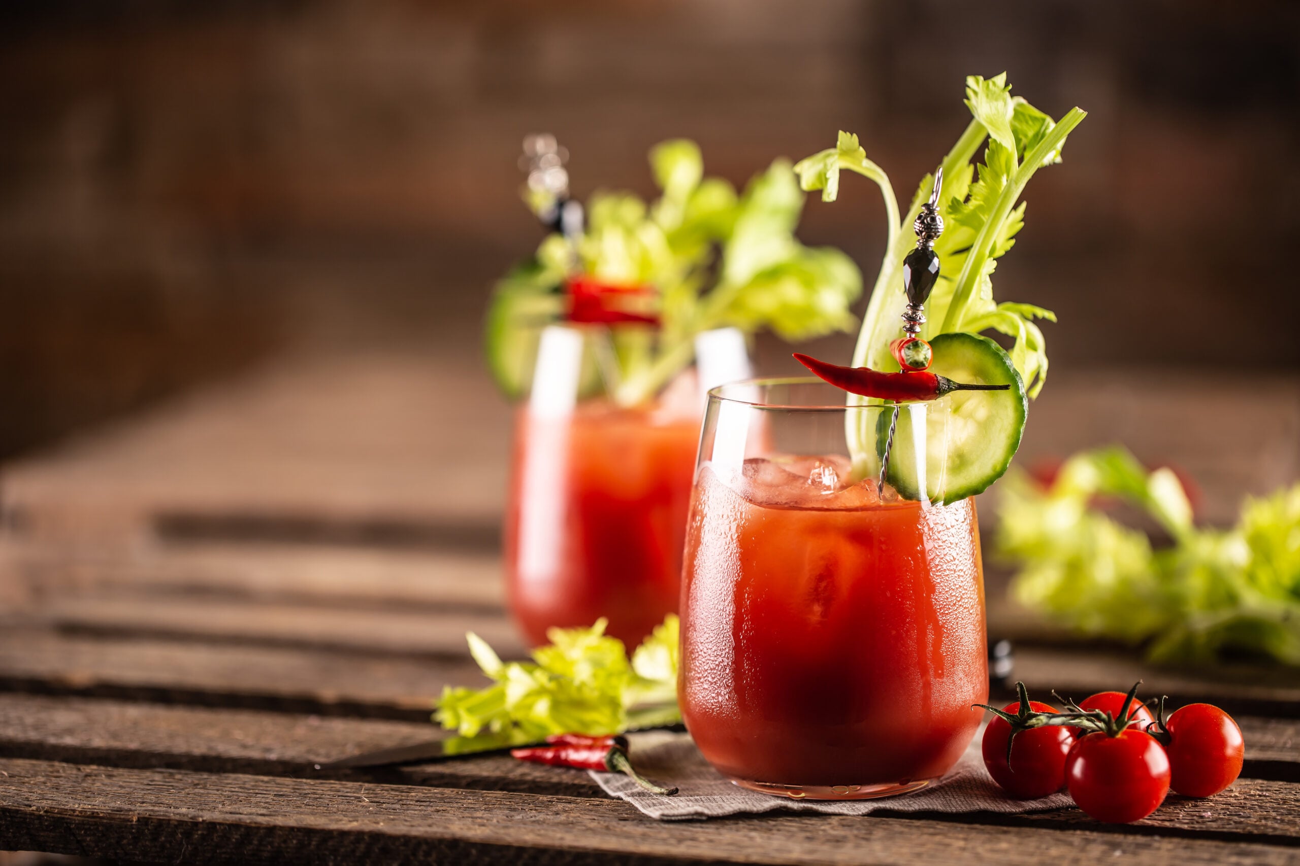 A wooden table featuring two glasses of Virgin Mary mocktails and their ingredients. 