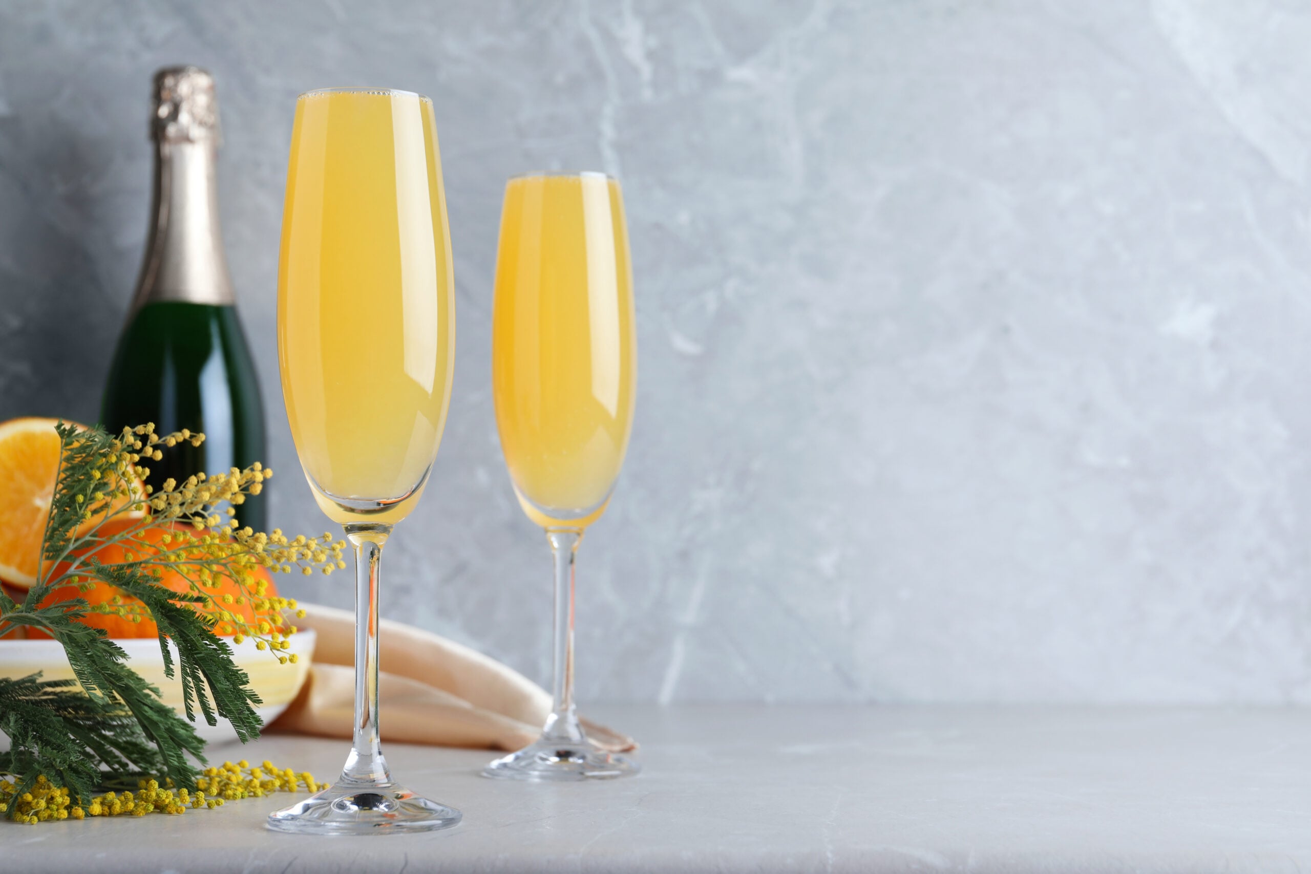 Two glasses of Mimosa, accompanied by its components.