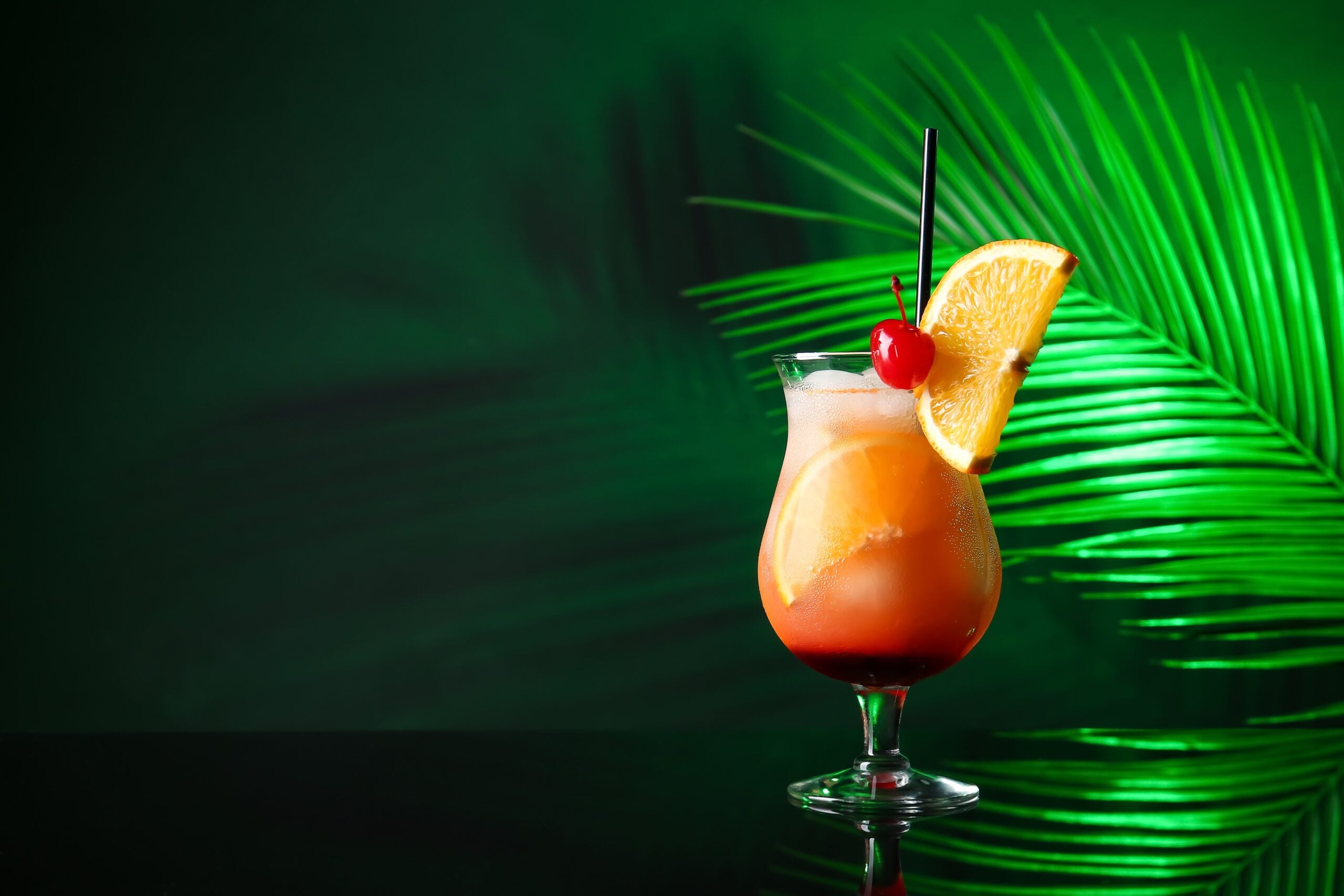 A glass of tasty Tequila Sunrise cocktail and palm leaves on a dark background