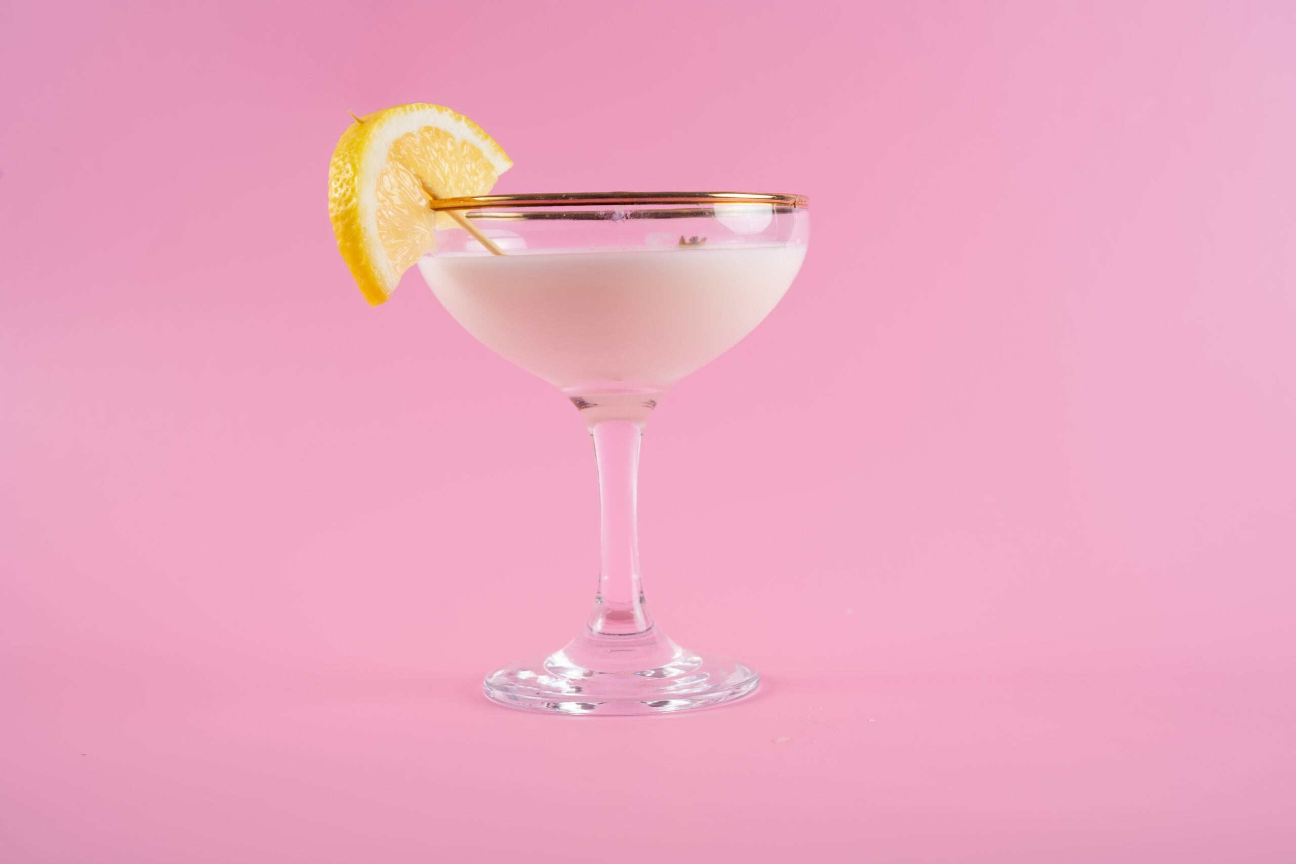 An isolated glass of tuxedo cocktail against a plain pink backdrop.
