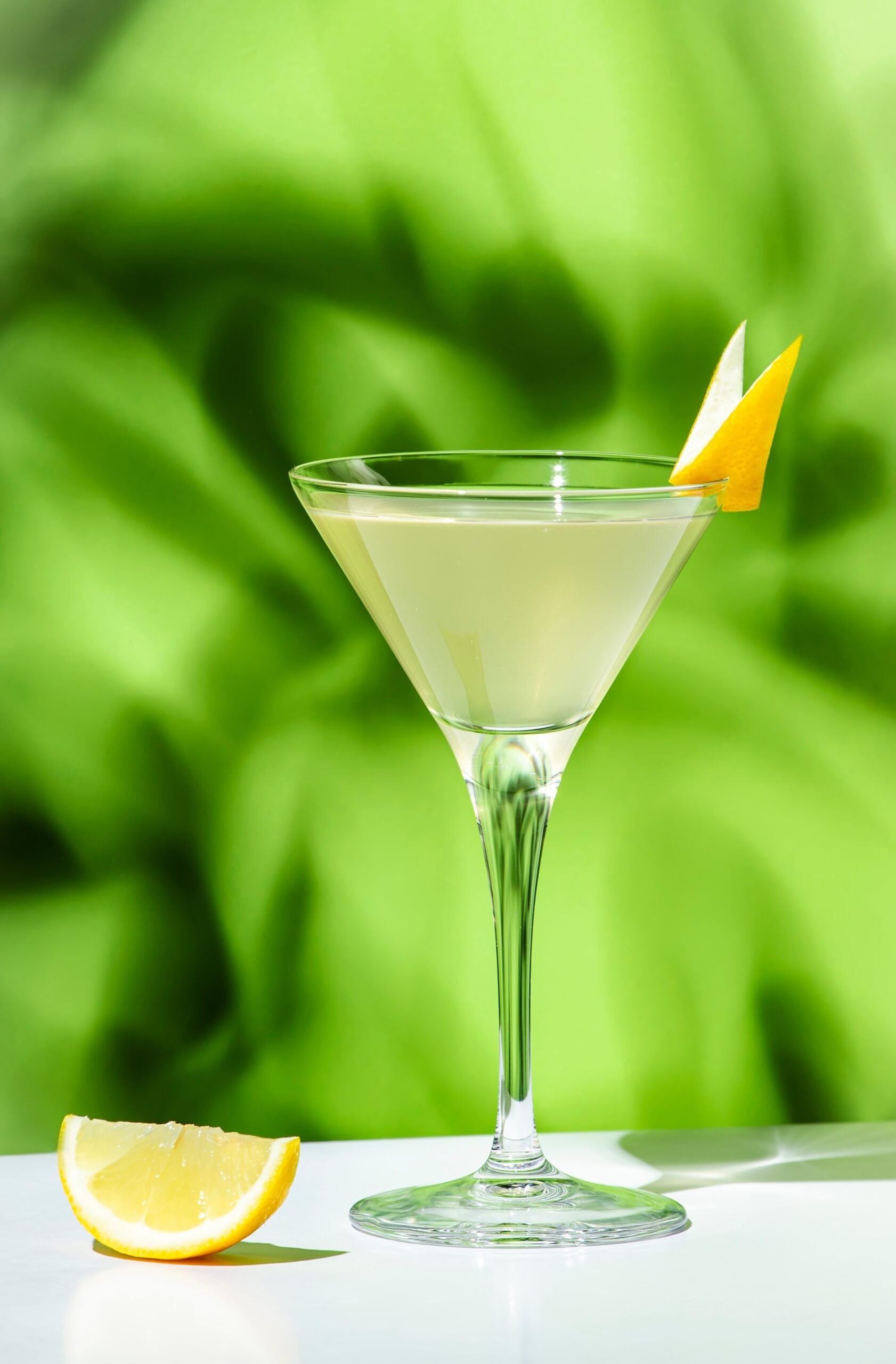A glass of Vesper Martini against a blurred, green backdrop. 
