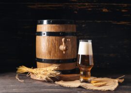 Wooden barrel with tap, beer glass, wheat stalks on burlap.