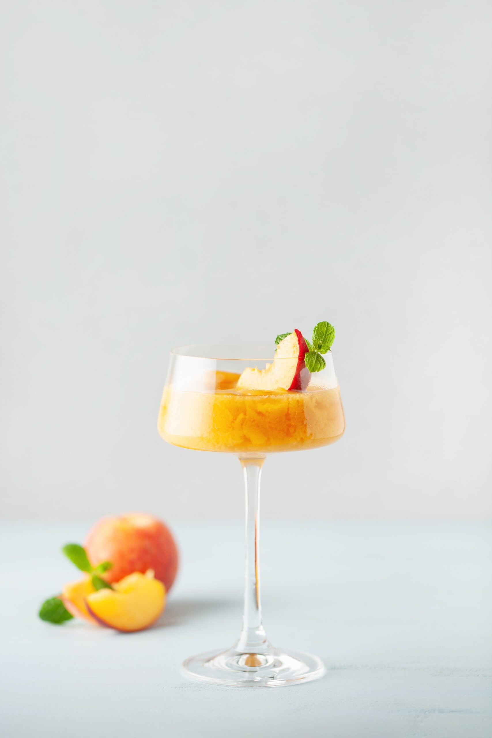 An isolated glass of peach Bellini, accompanied by fresh peaches. 