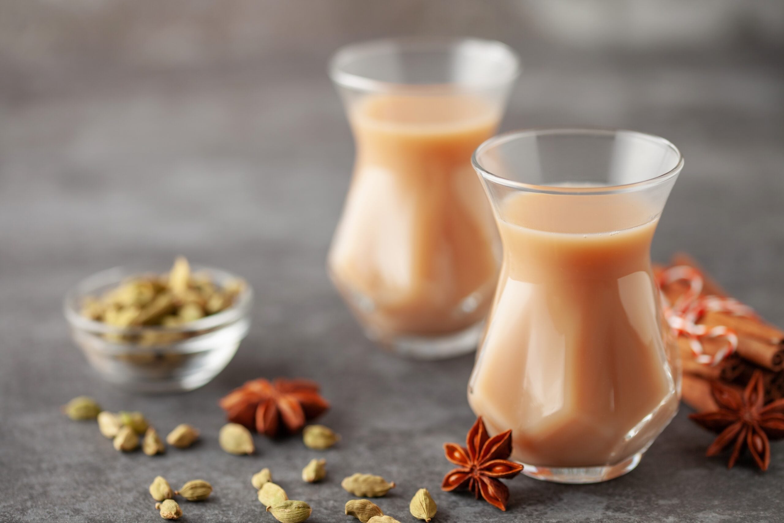 Two cups of Karak chai tea encircled by its ingredients. 