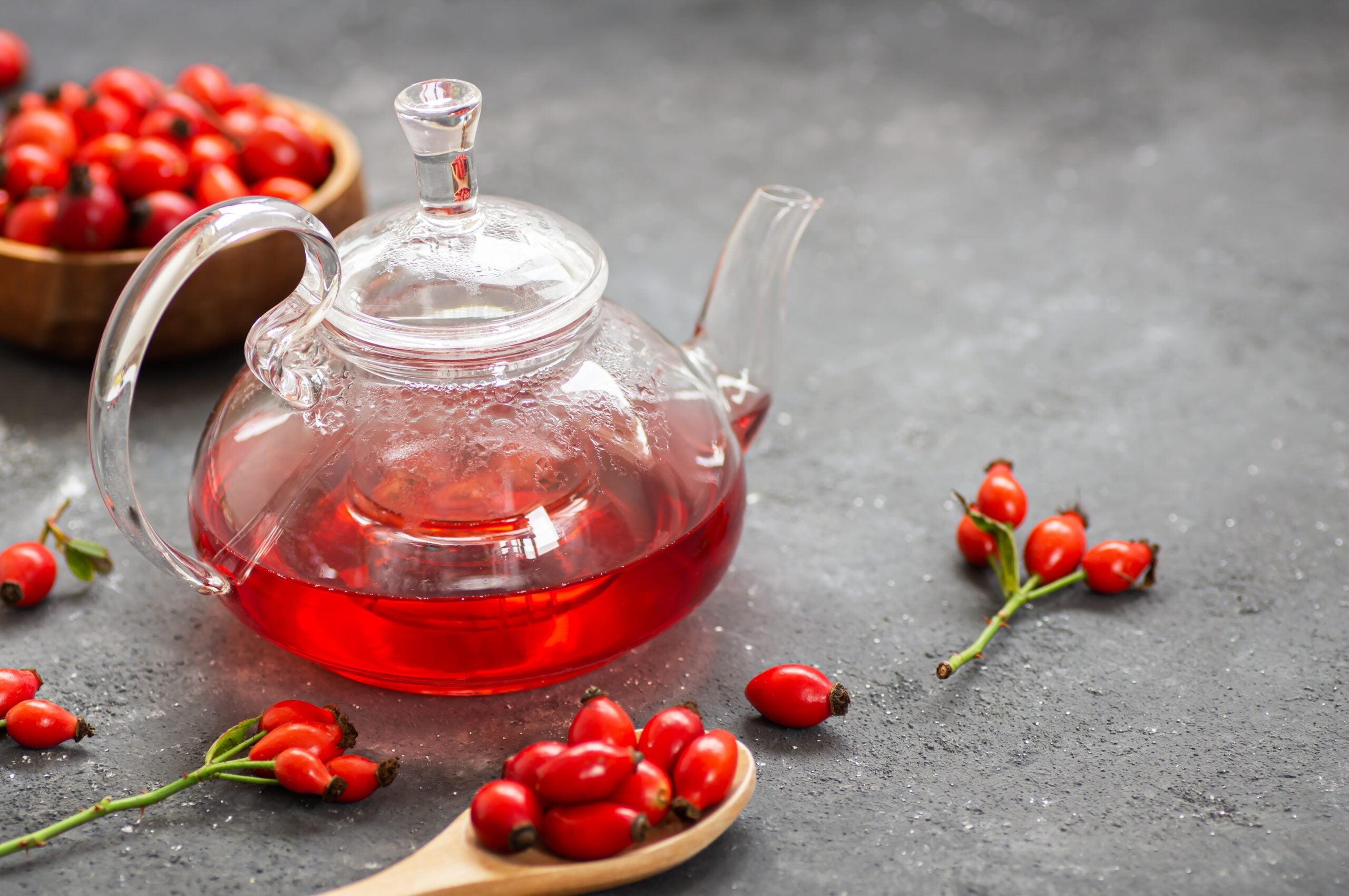 A teapot filled with freshly made rosehip tea and some ripe rosehip fruits. 
