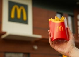 Hand holding a McDonald's container of fries next to a McDonald's sign