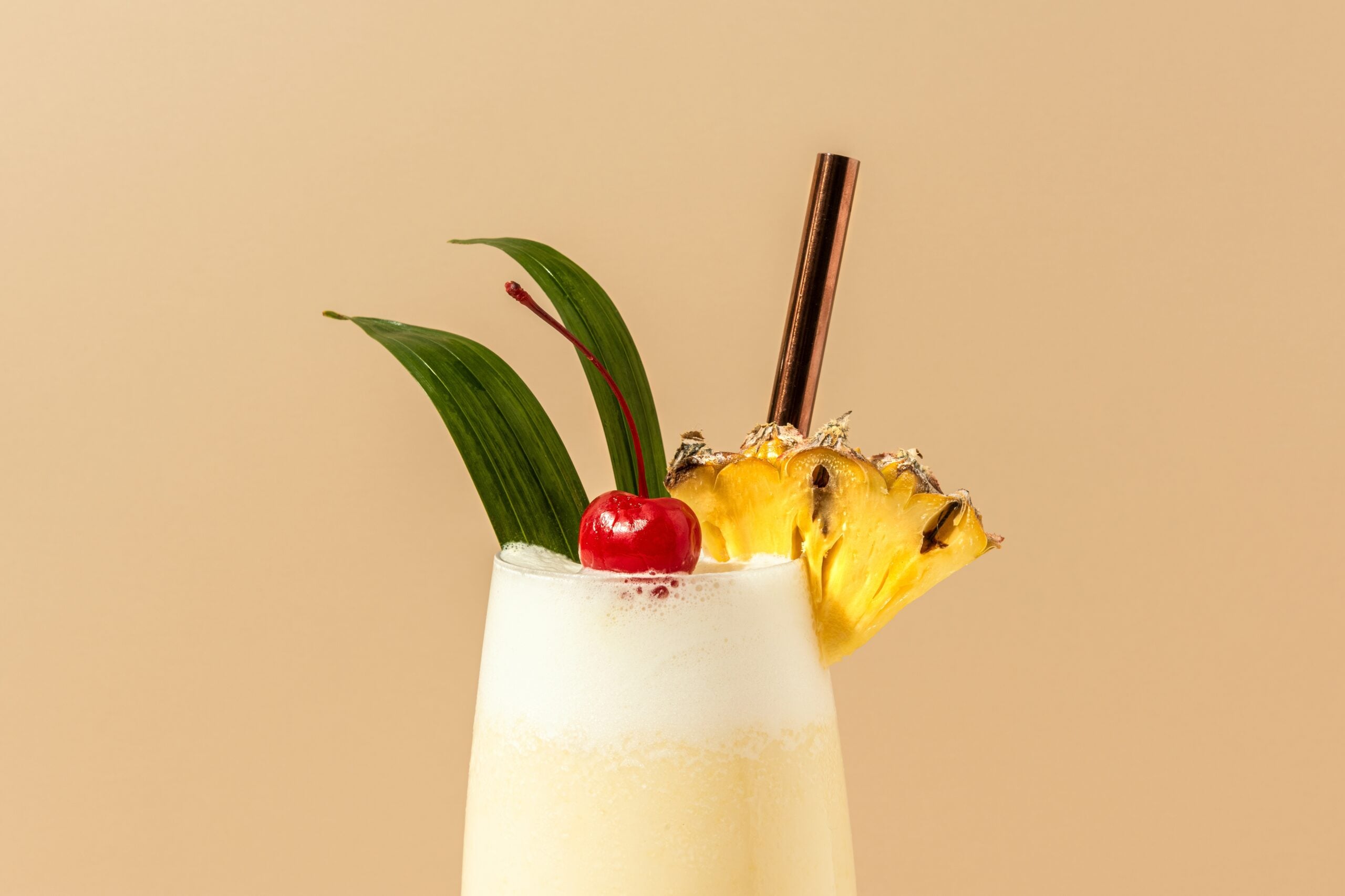 A macro shot of pina colada garnished with pineapple and a cherry. 