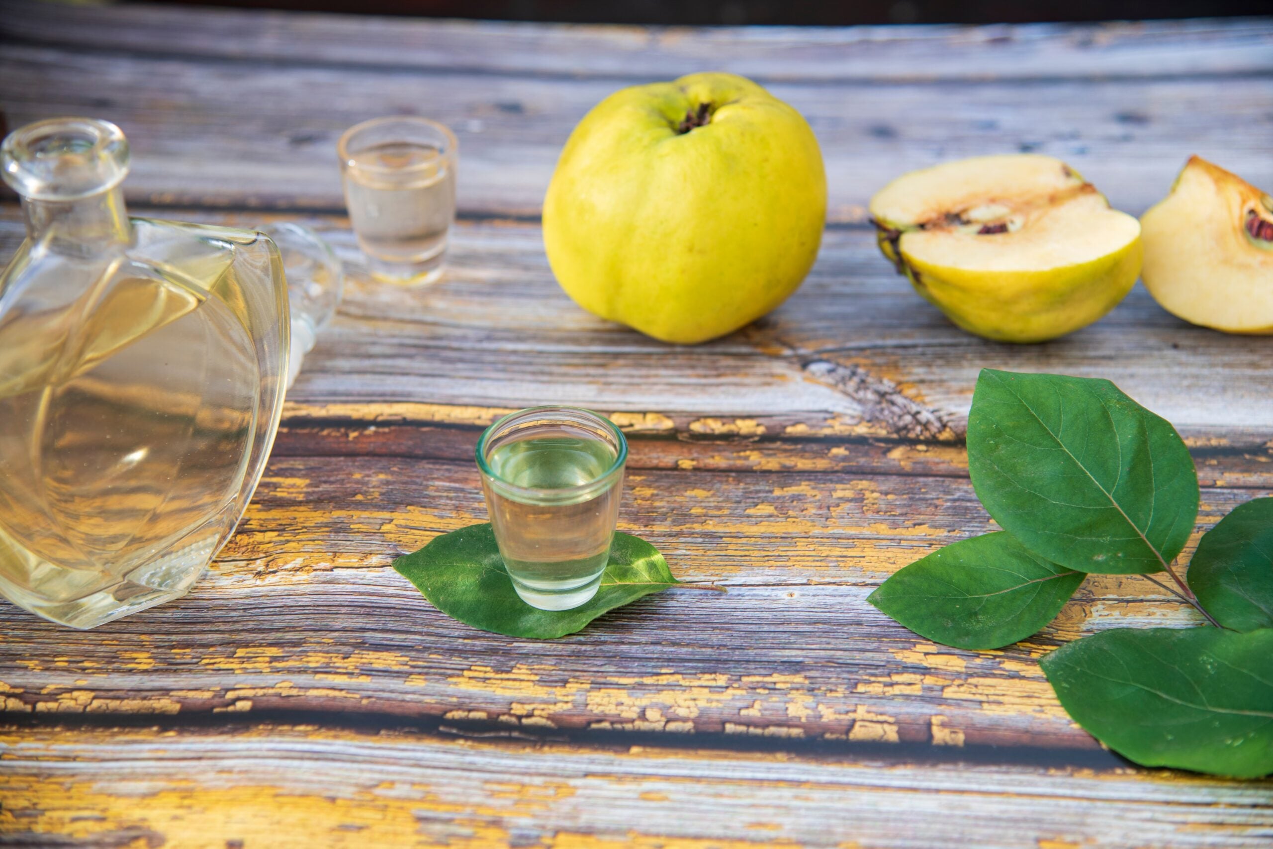 A weathered wooden table showcasing quince brandy and some fresh quinces. 