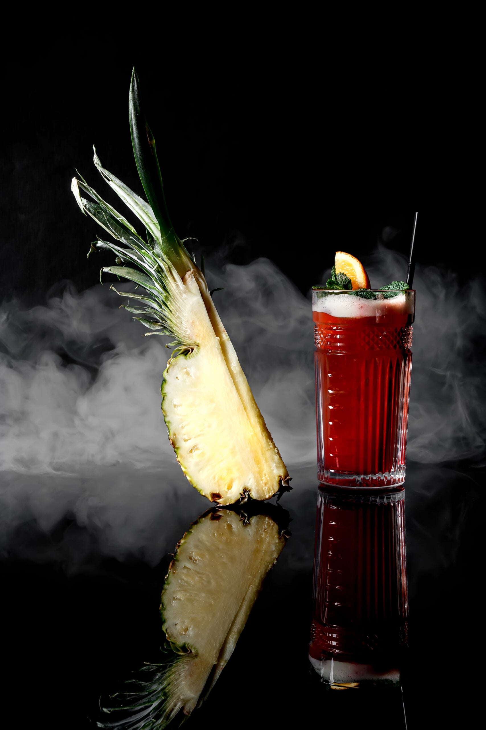 A glass of Planter's Punch cocktail and a slice of pineapple on a black background. 
