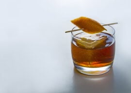 Glass of whiskey with ice and orange peel garnish.